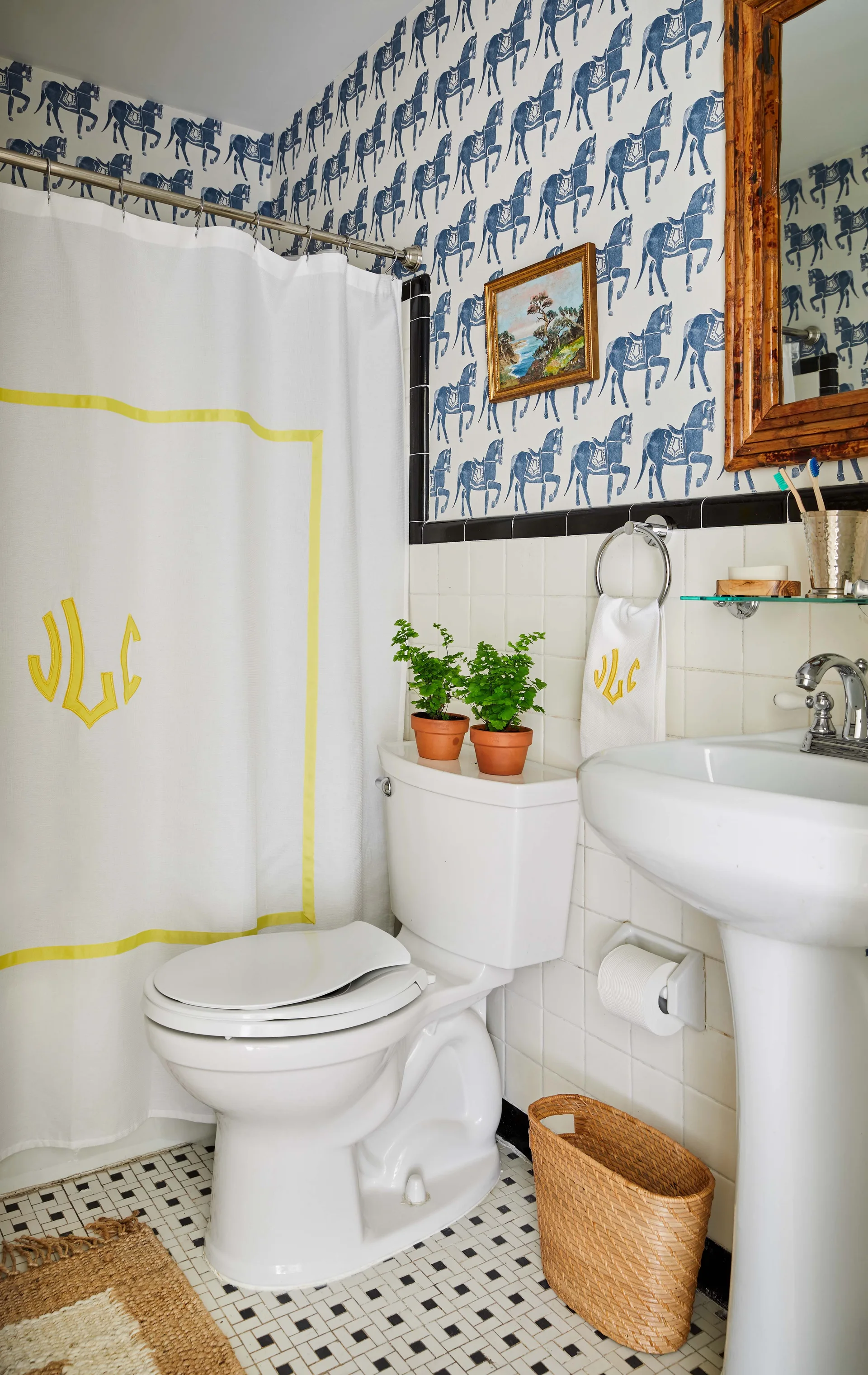 A compact bathroom features blue and white horse-patterned wallpaper, white square wall tiles, a white pedestal sink, and a toilet.