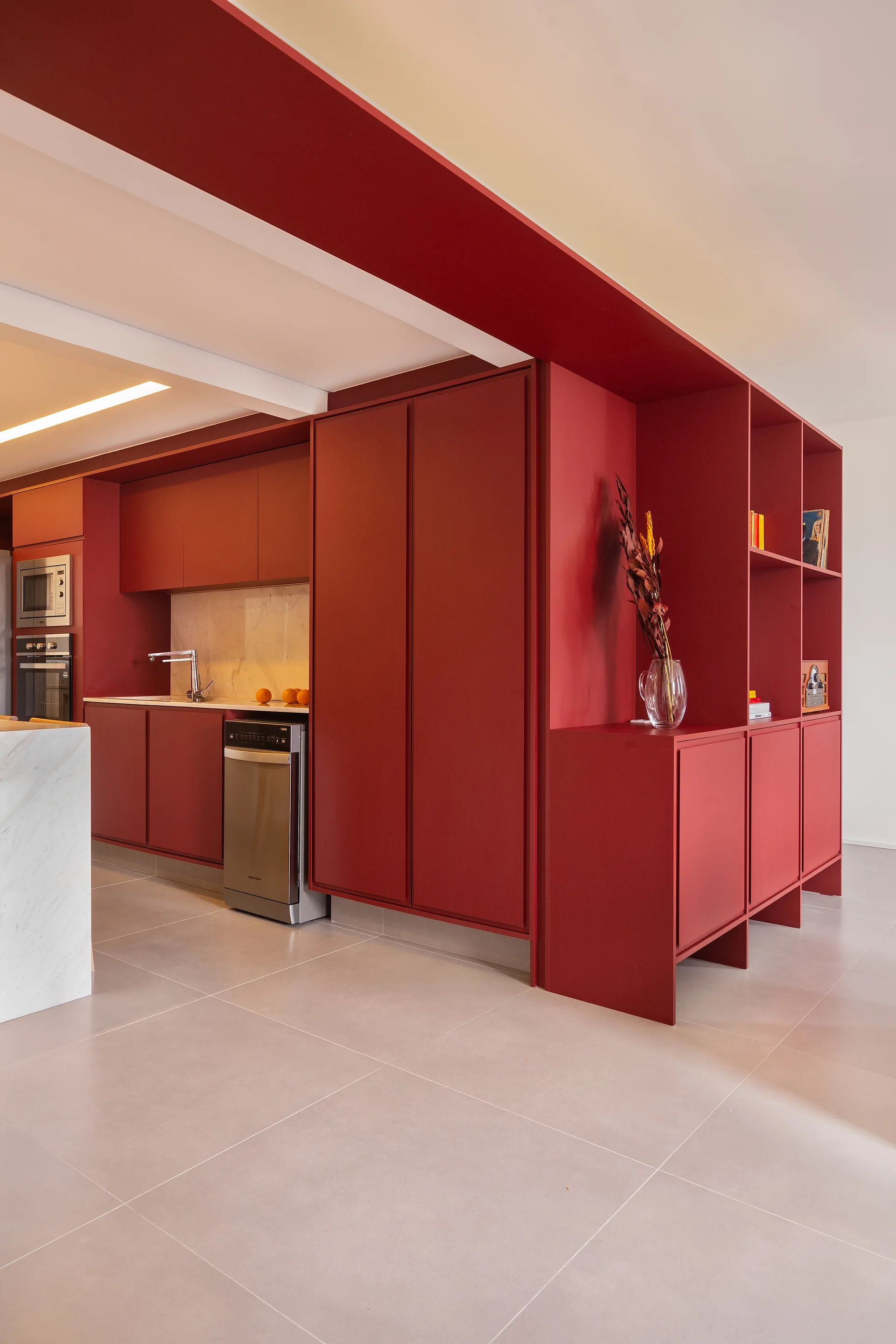 A modern kitchen with matte red floor-to-ceiling cabinets, a white marble backsplash, a matching island, and light grey tile floors.