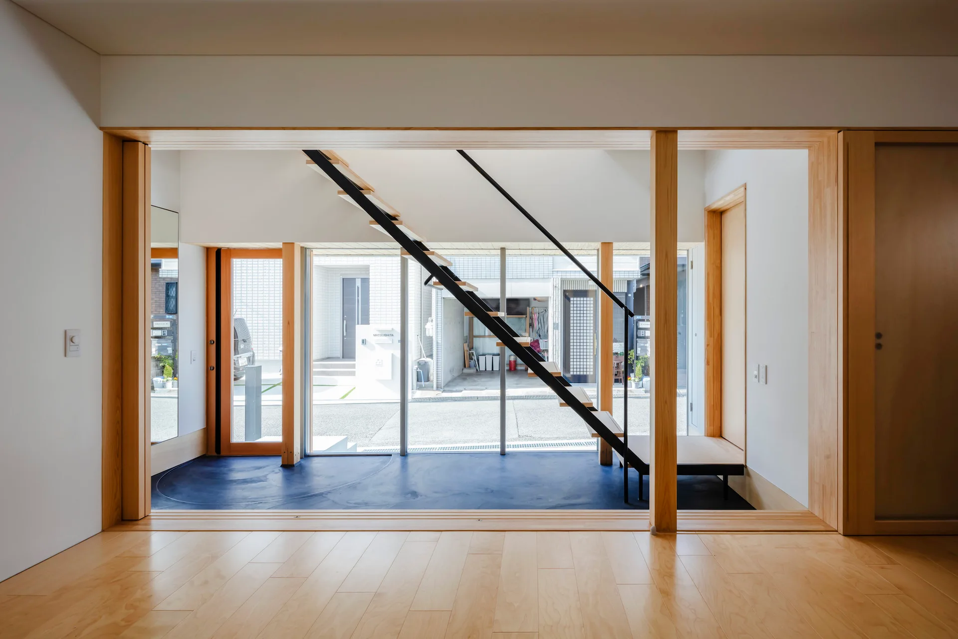 A minimalist entryway features a floating black metal staircase with wooden treads in front of a floor-to-ceiling glass wall.