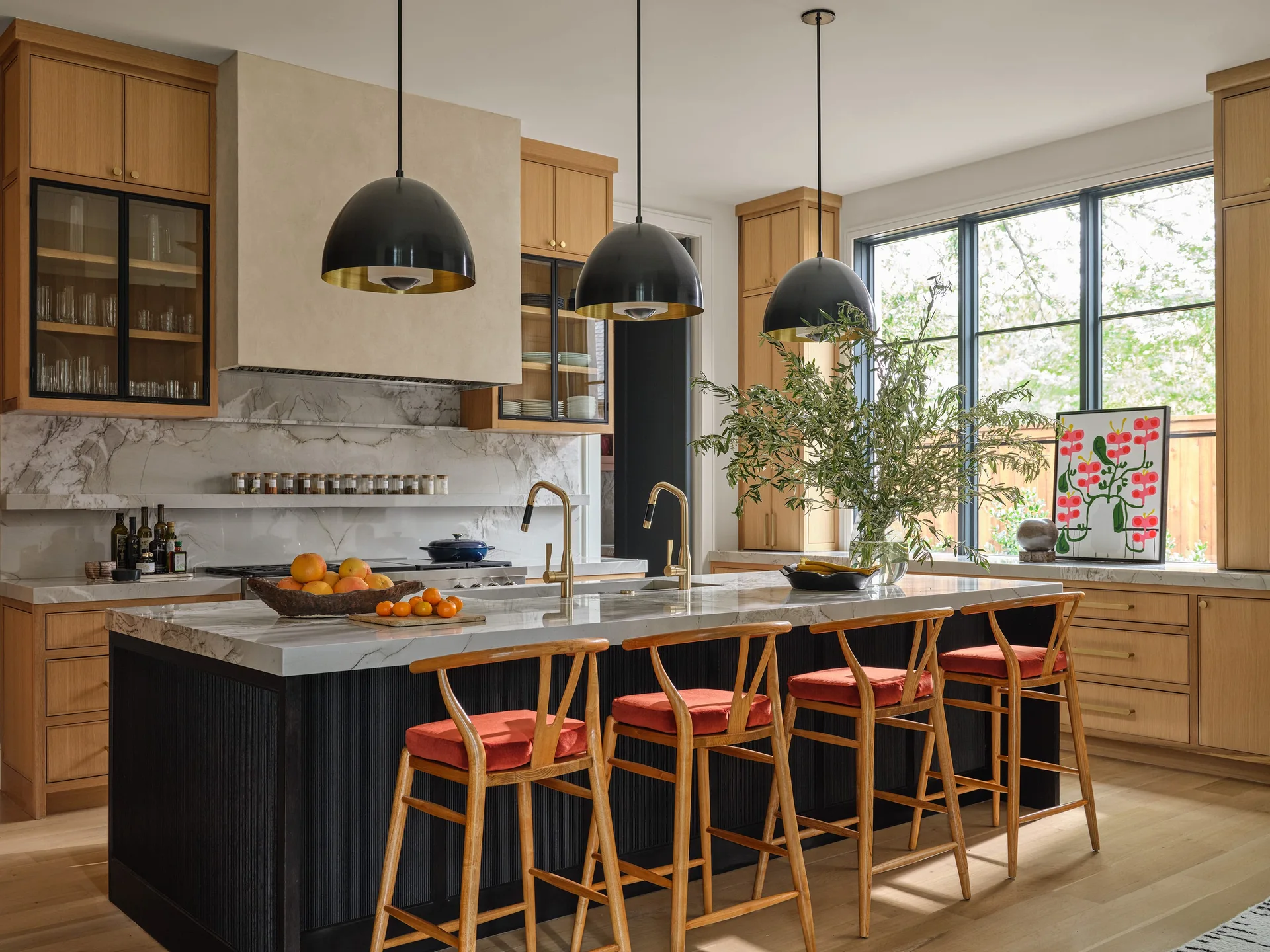 A modern residential kitchen features a black fluted island with a marble countertop, light wood cabinetry, and three large black dome pendant lights.