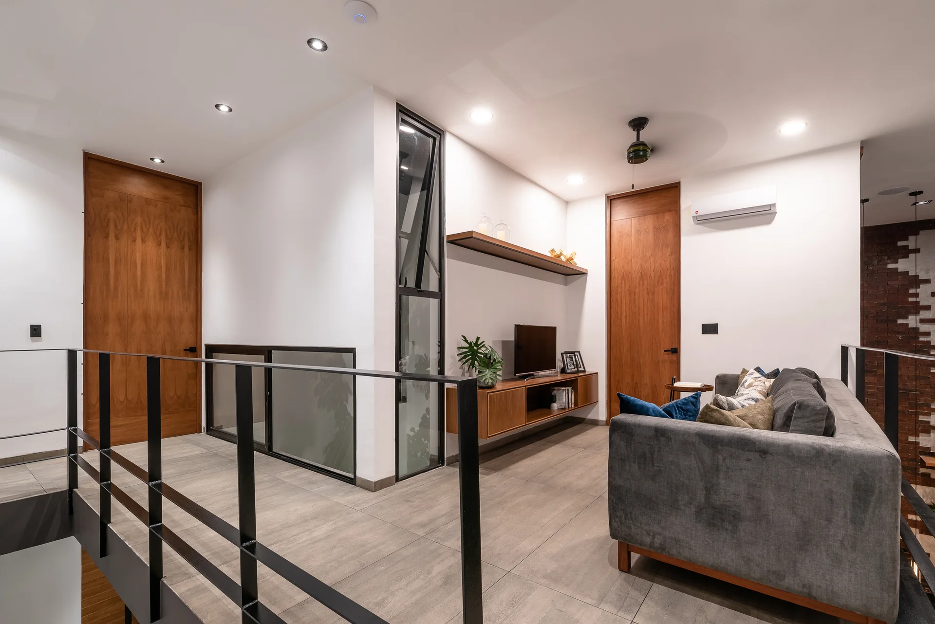 A modern residential landing featuring a gray sofa, a floating wood media console, matching doors, and black metal railings.