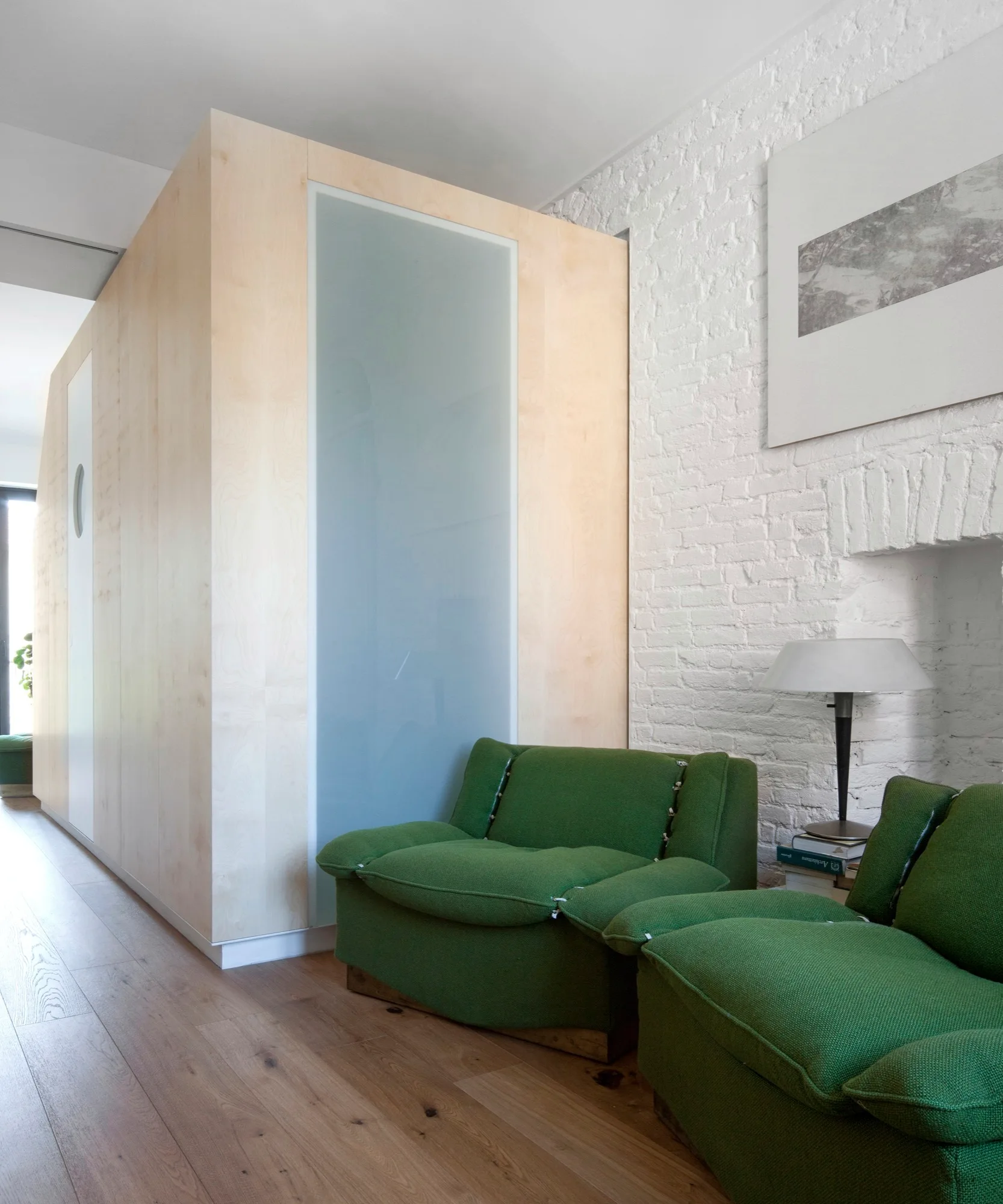 Two plush green armchairs sit in front of a white painted brick wall and a light wood partition with a frosted glass panel.
