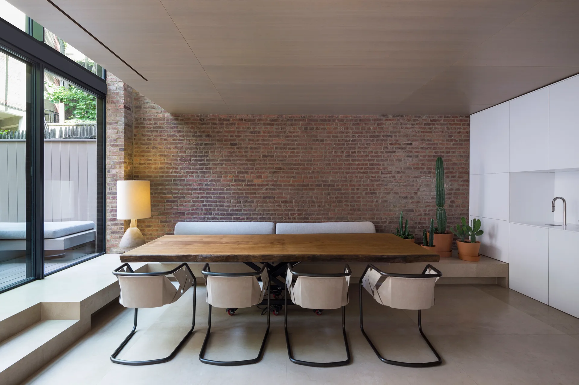 A modern dining room with a live-edge wooden table, modern chairs, a low stone bench, and an exposed brick wall.