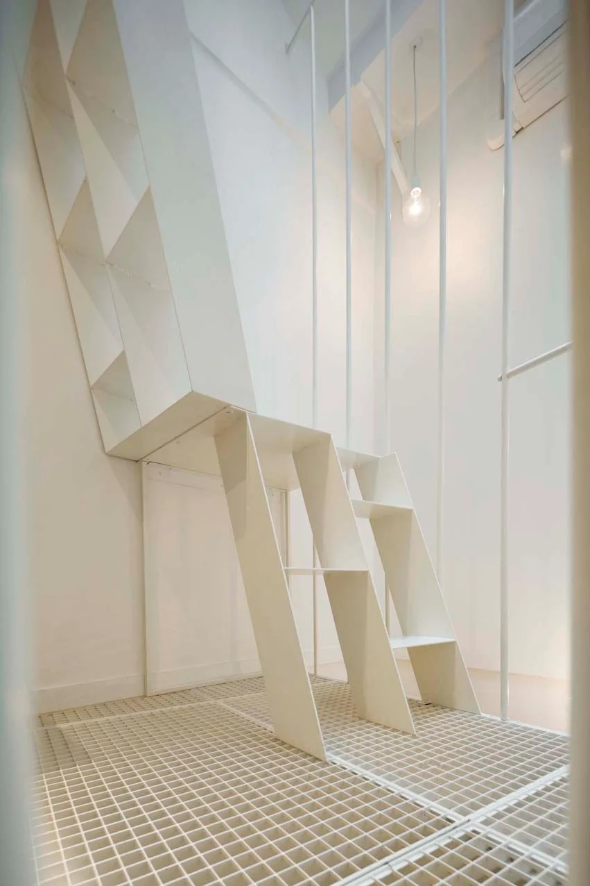 A modern white interior features a geometric sculptural staircase, vertical rod railings, and an industrial-style gridded metal floor.