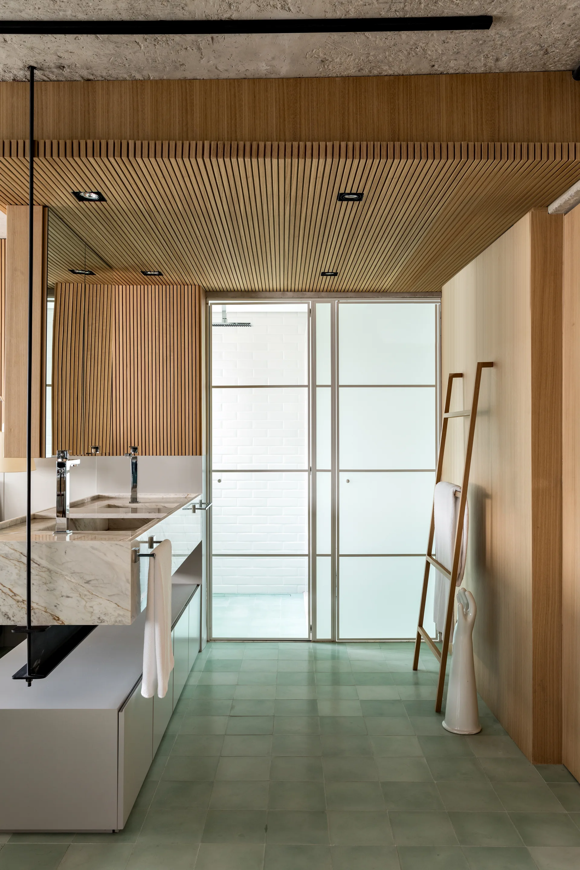 A modern bathroom with a double marble vanity, a slatted wood ceiling, light green floor tiles, and a wooden towel ladder against the wall.