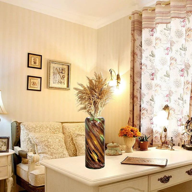 A cream-colored desk holds a patterned vase with dried decorative stems in a room with a patterned sofa and curtains.