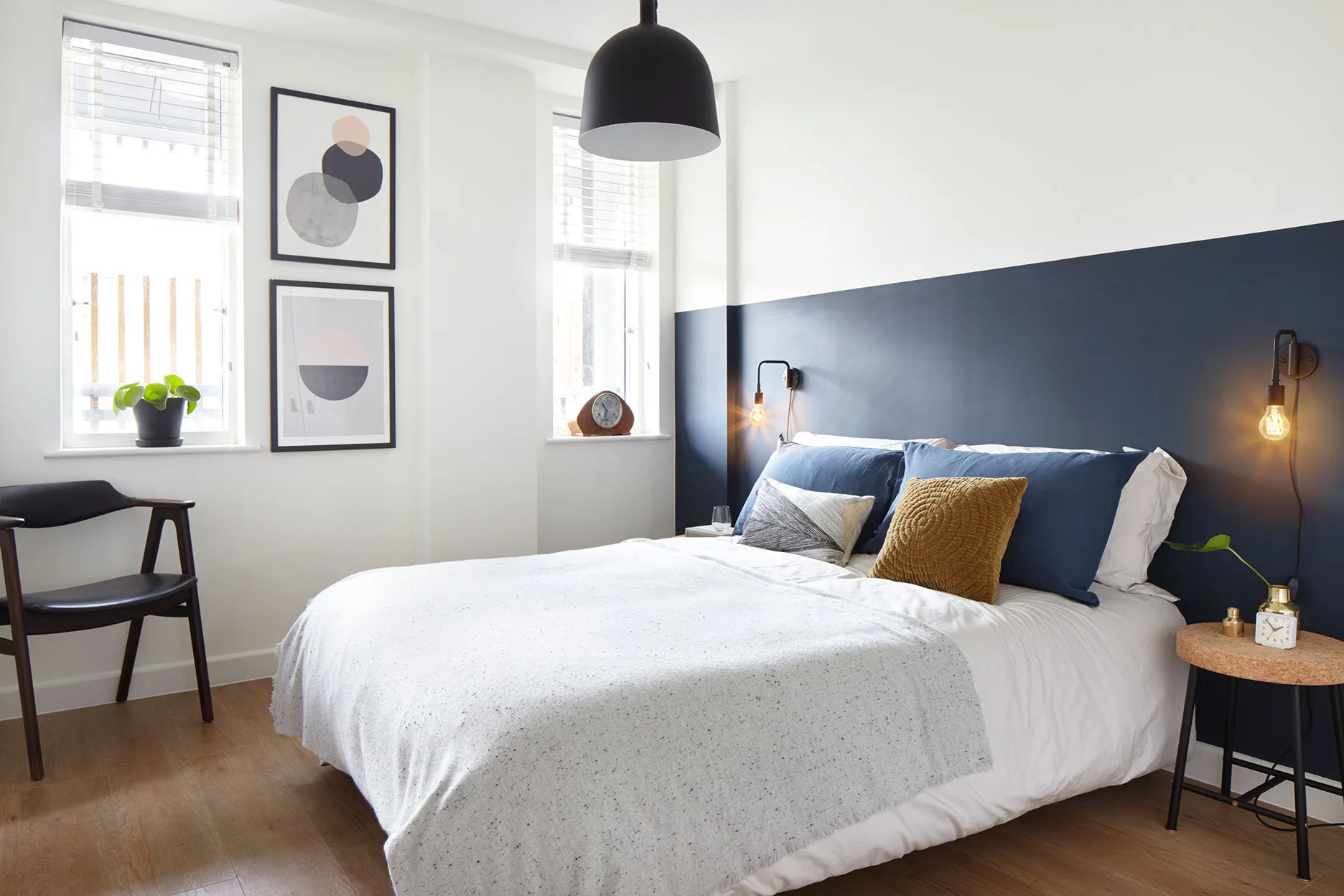 A modern bedroom features a two-tone navy and white accent wall behind a bed next to a cork side table.