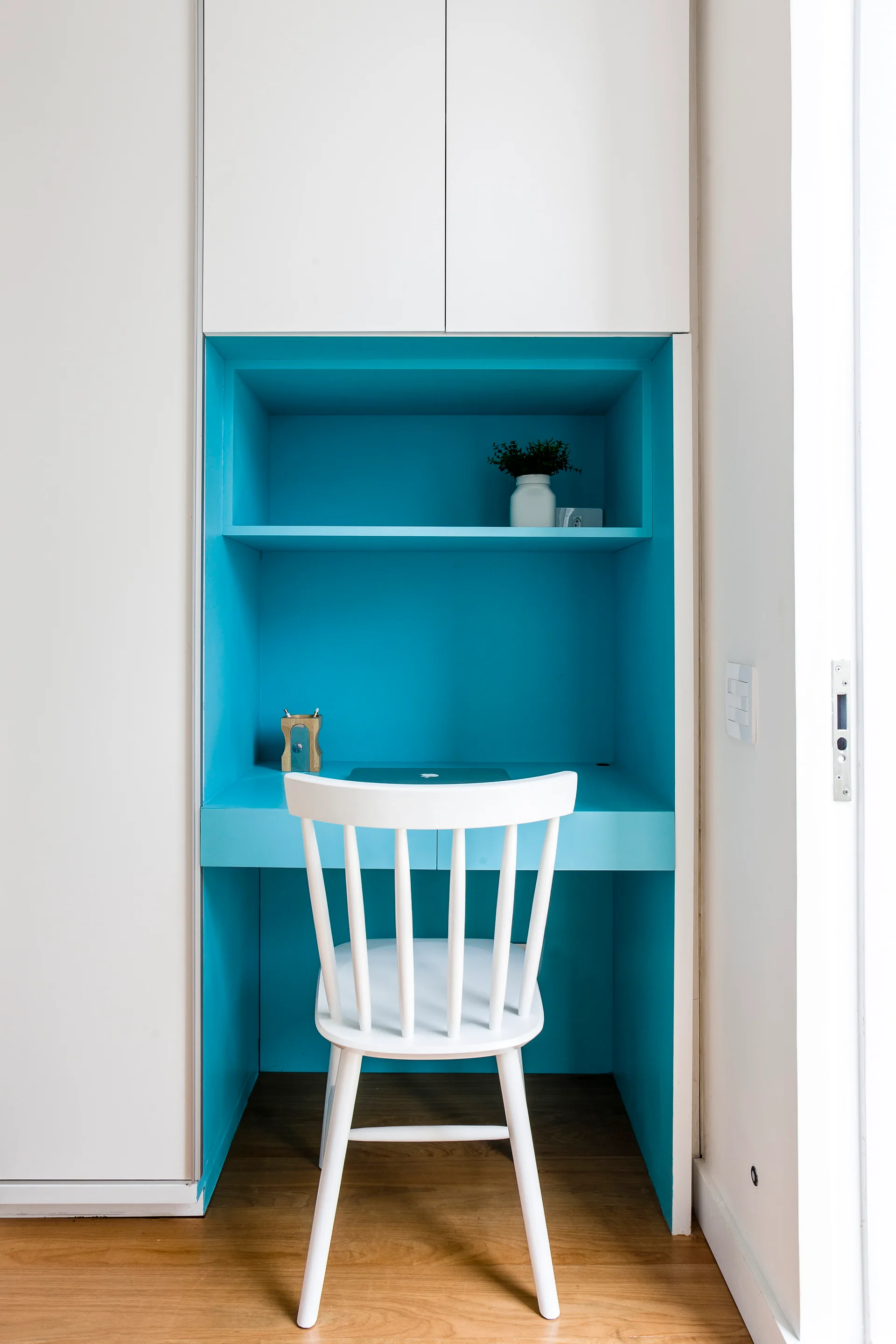 A blue built-in desk niche is integrated into white cabinetry and features a matching white wooden spindle chair.