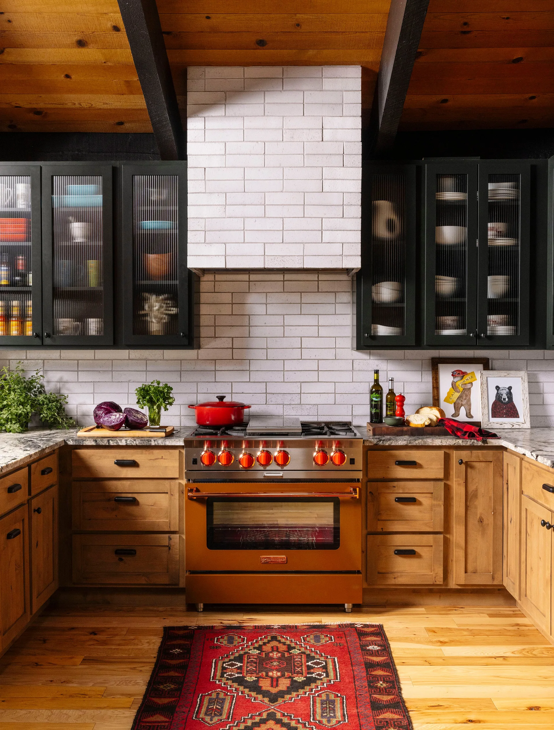 A rustic kitchen features wood base cabinets, black upper cabinets with reeded glass doors, a copper range, and a white tiled vent hood.