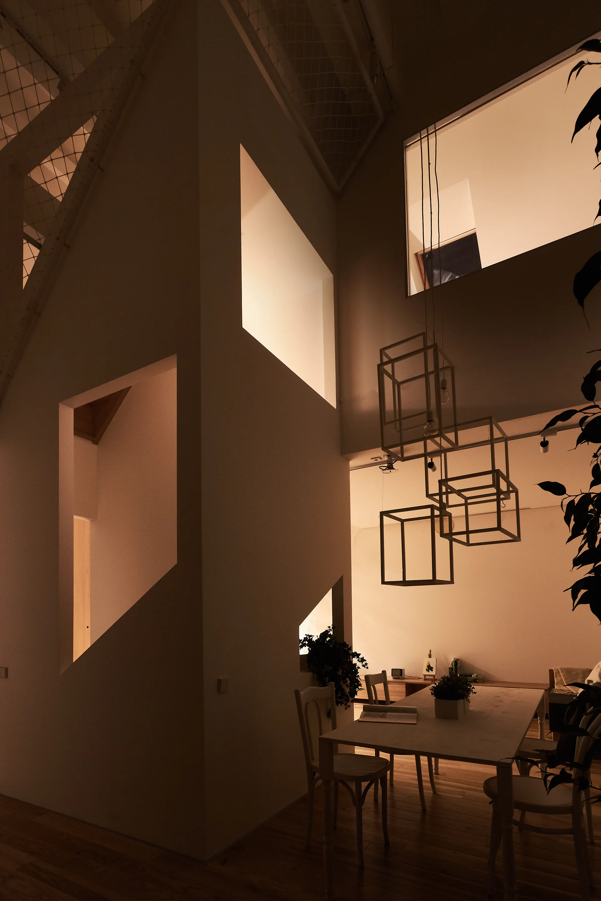 A minimalist dining room with a wooden table, wireframe pendant lights, and large geometric cutouts in the walls.