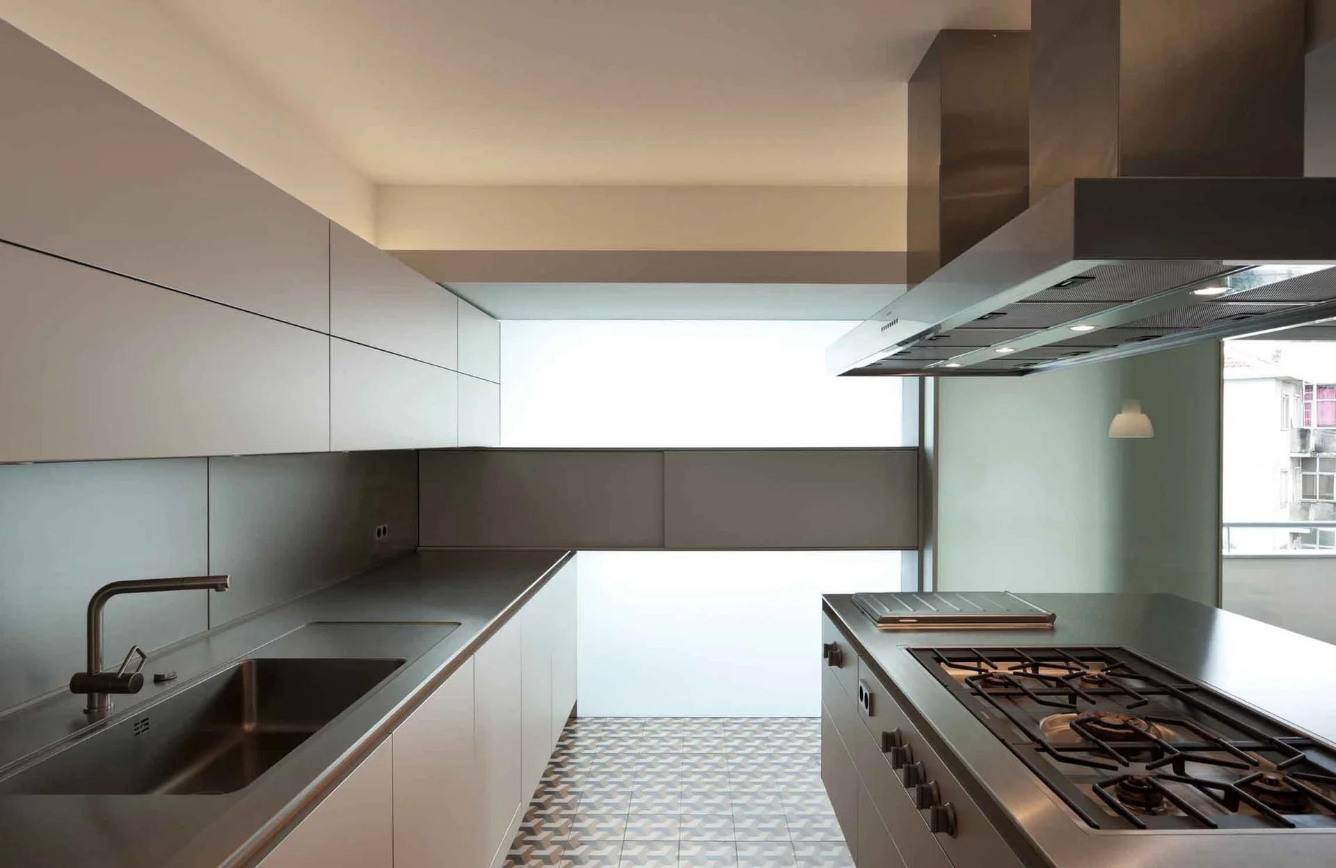 A modern minimalist kitchen with flat-panel cabinets, integrated stainless steel sink, gas cooktop, and patterned geometric floor tiles.