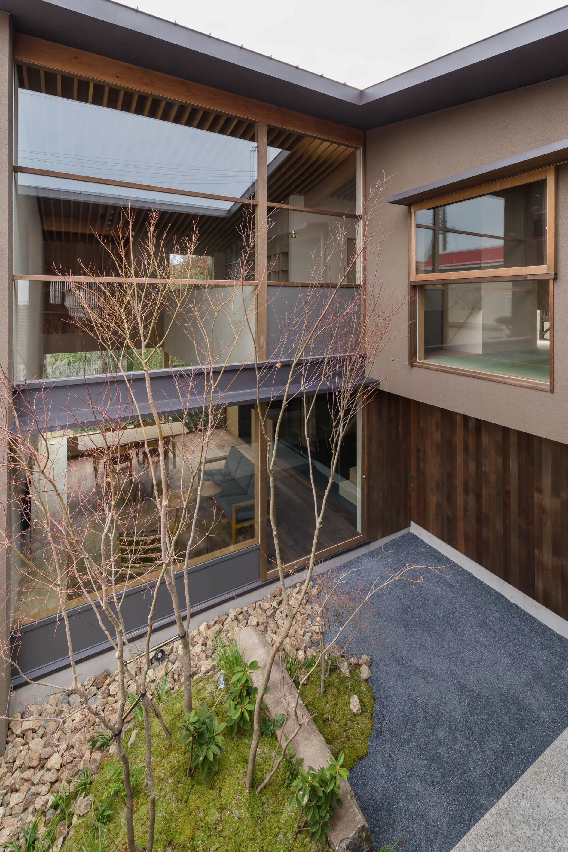 A modern courtyard features a mossy rock garden with thin bare trees, viewed through a multi-story glass facade.