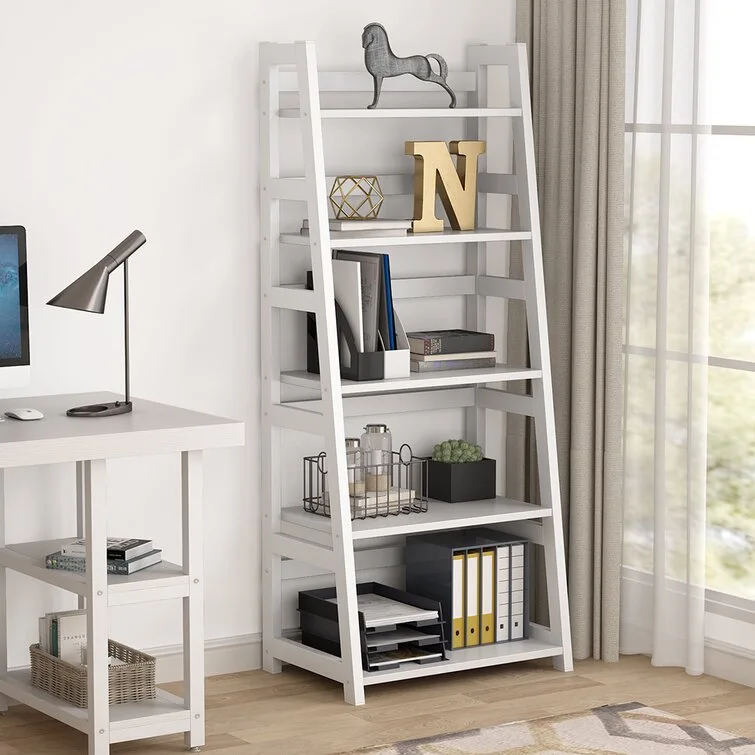 A white ladder-style bookshelf decorated with storage binders and small gold accents stands next to a matching white desk.