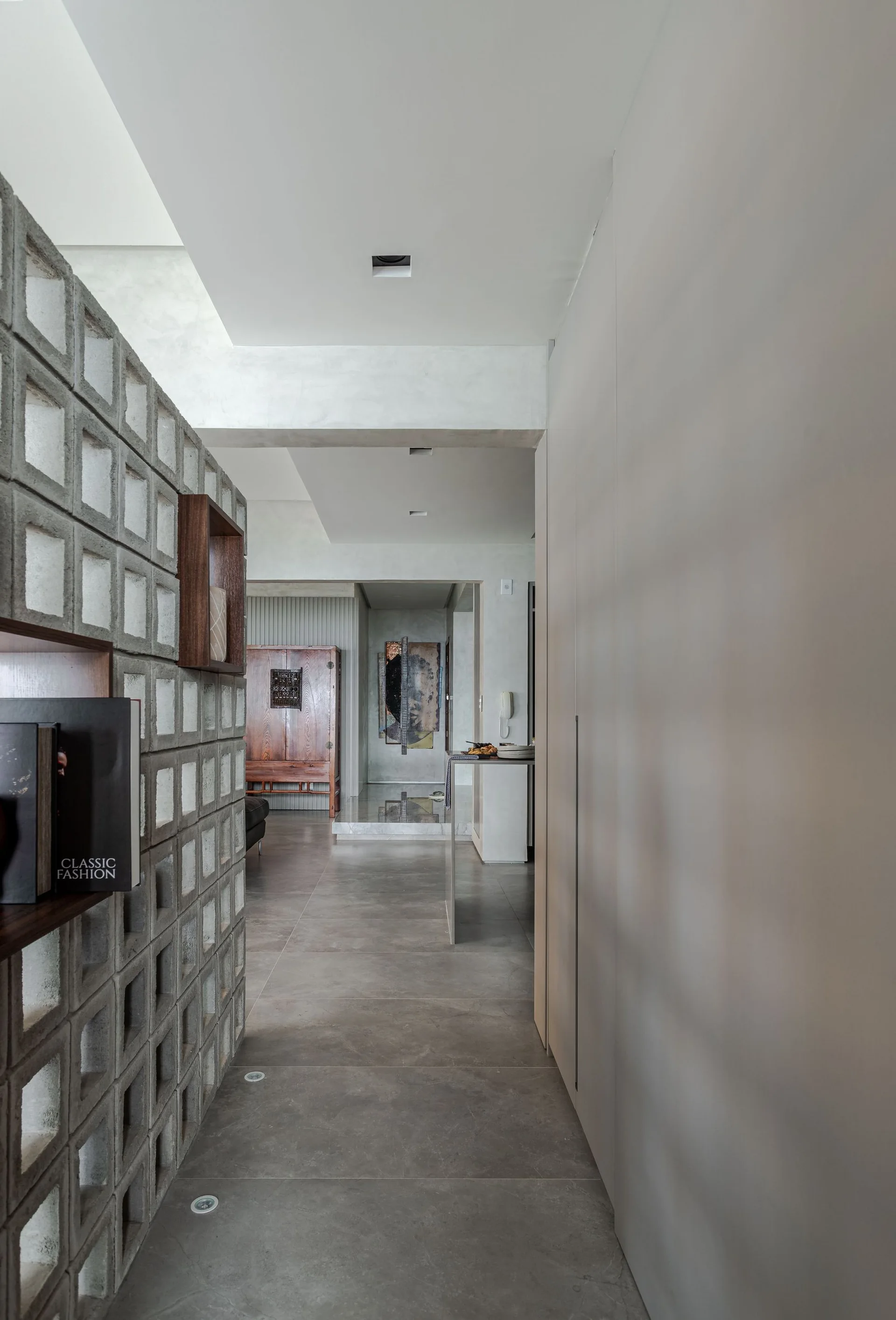 A gray hallway features a concrete breeze block screen wall with wooden display inserts on the left and smooth floor-to-ceiling cabinetry on the right.
