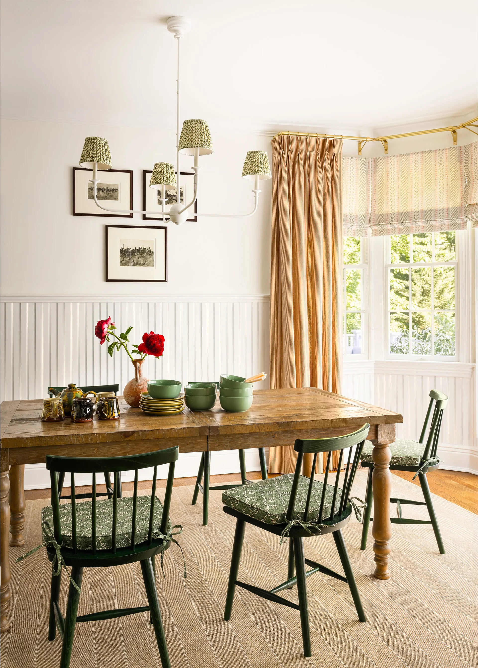 A cottage-style dining room features a rustic wooden table surrounded by green spindle-back chairs on a textured tan rug.