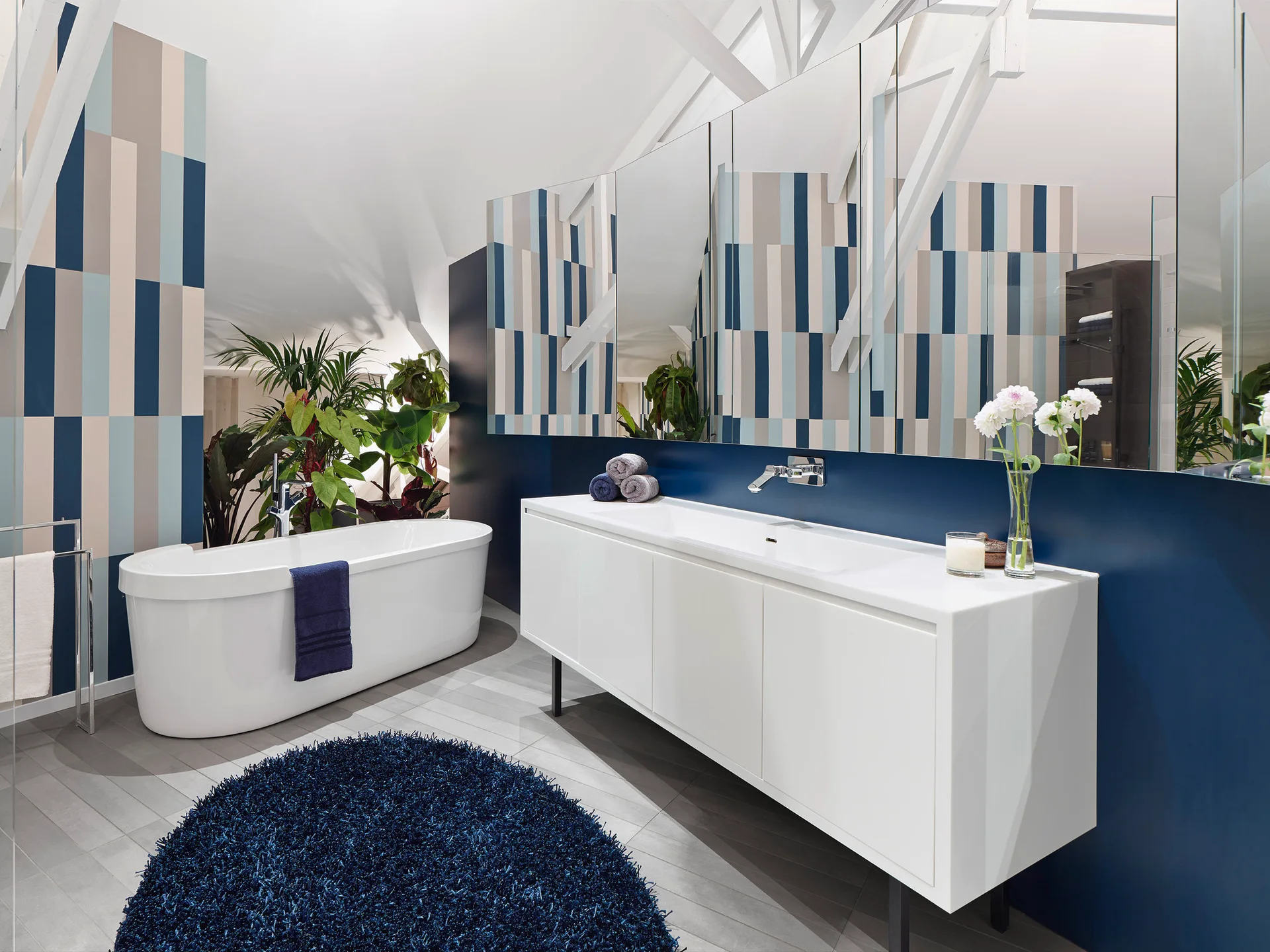 A modern attic bathroom featuring a white freestanding bathtub, a sleek vanity, and a navy blue geometric striped accent wall.
