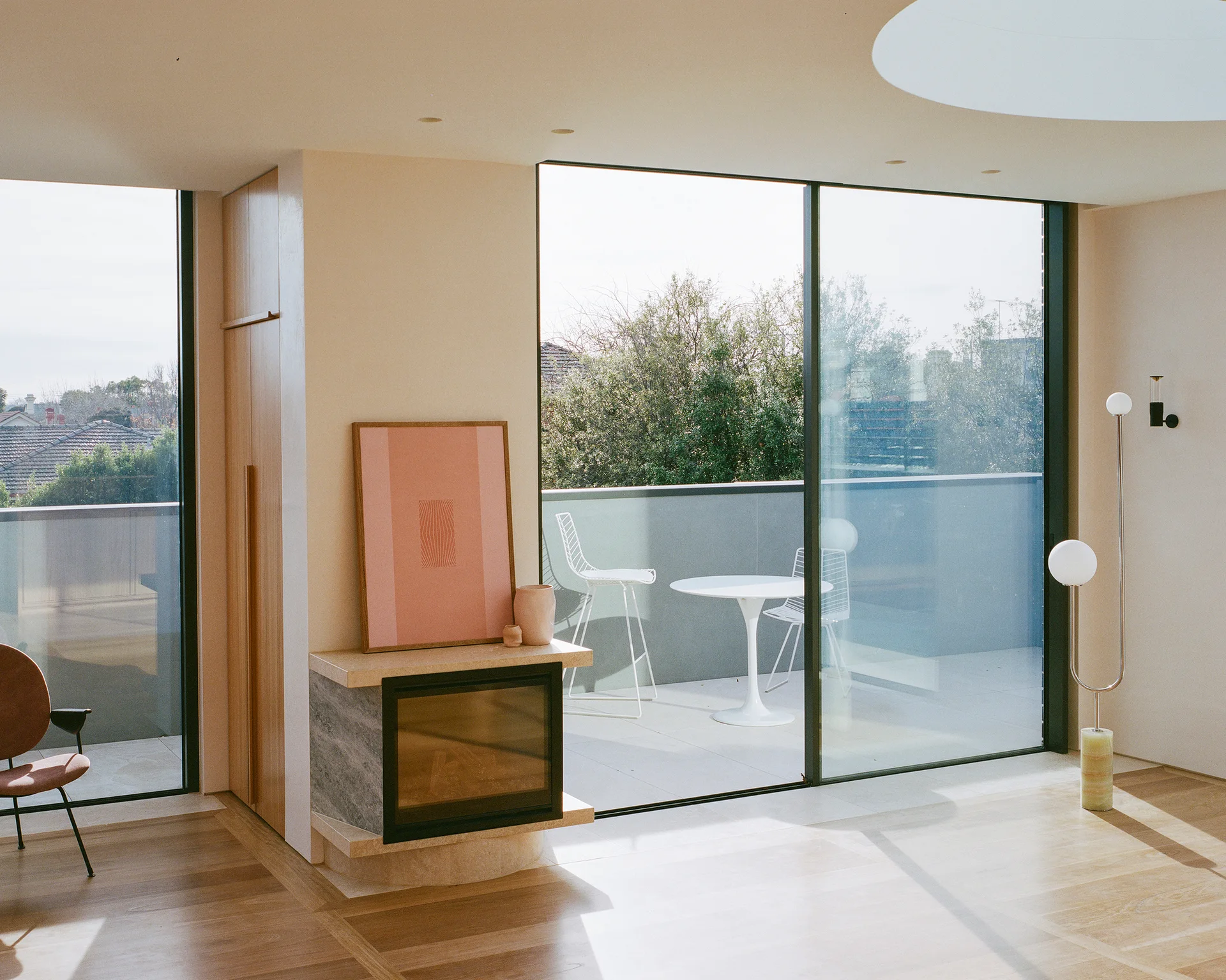 A minimalist living room features a stone fireplace with pink artwork, built-in wooden cabinets, and glass doors opening to a balcony.