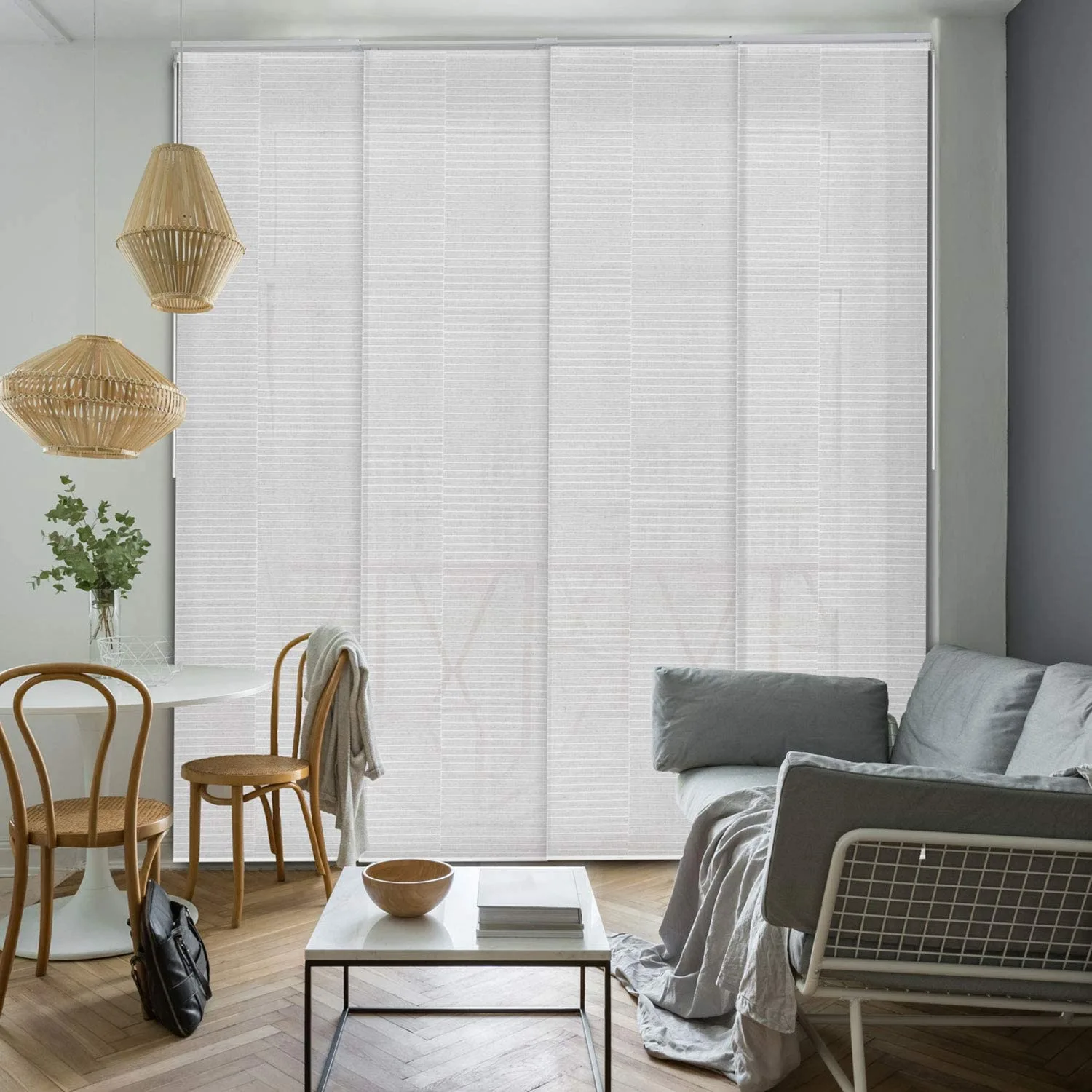 A light-filled living area featuring fabric panel track blinds, a grey sofa, a small dining nook, and herringbone wood flooring.