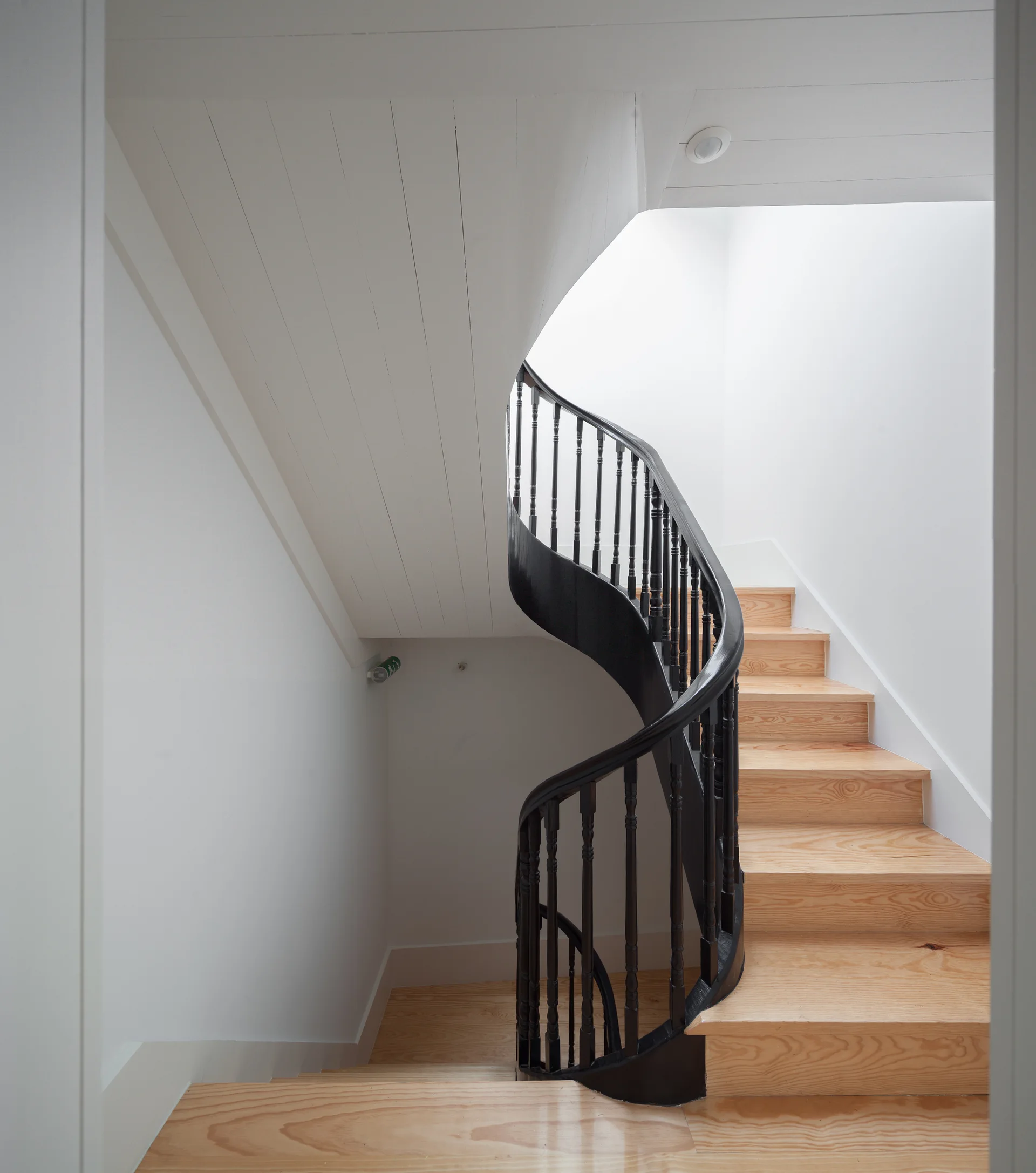 A curved staircase features light wood treads and a contrasting matte black railing against smooth white walls.