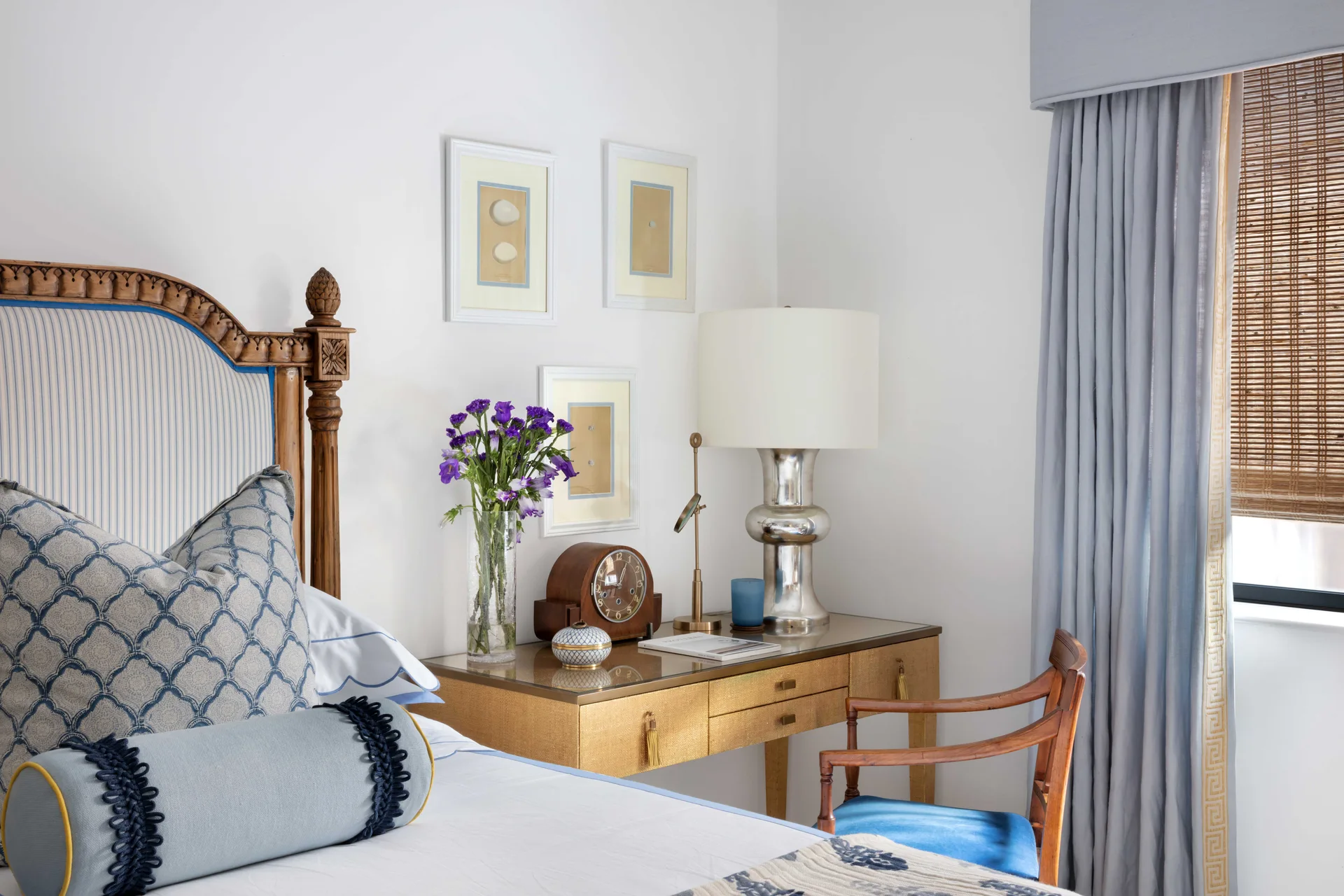 A bedroom corner features a carved wood headboard with blue striped fabric, a textured gold nightstand, a silver table lamp, and blue drapes.