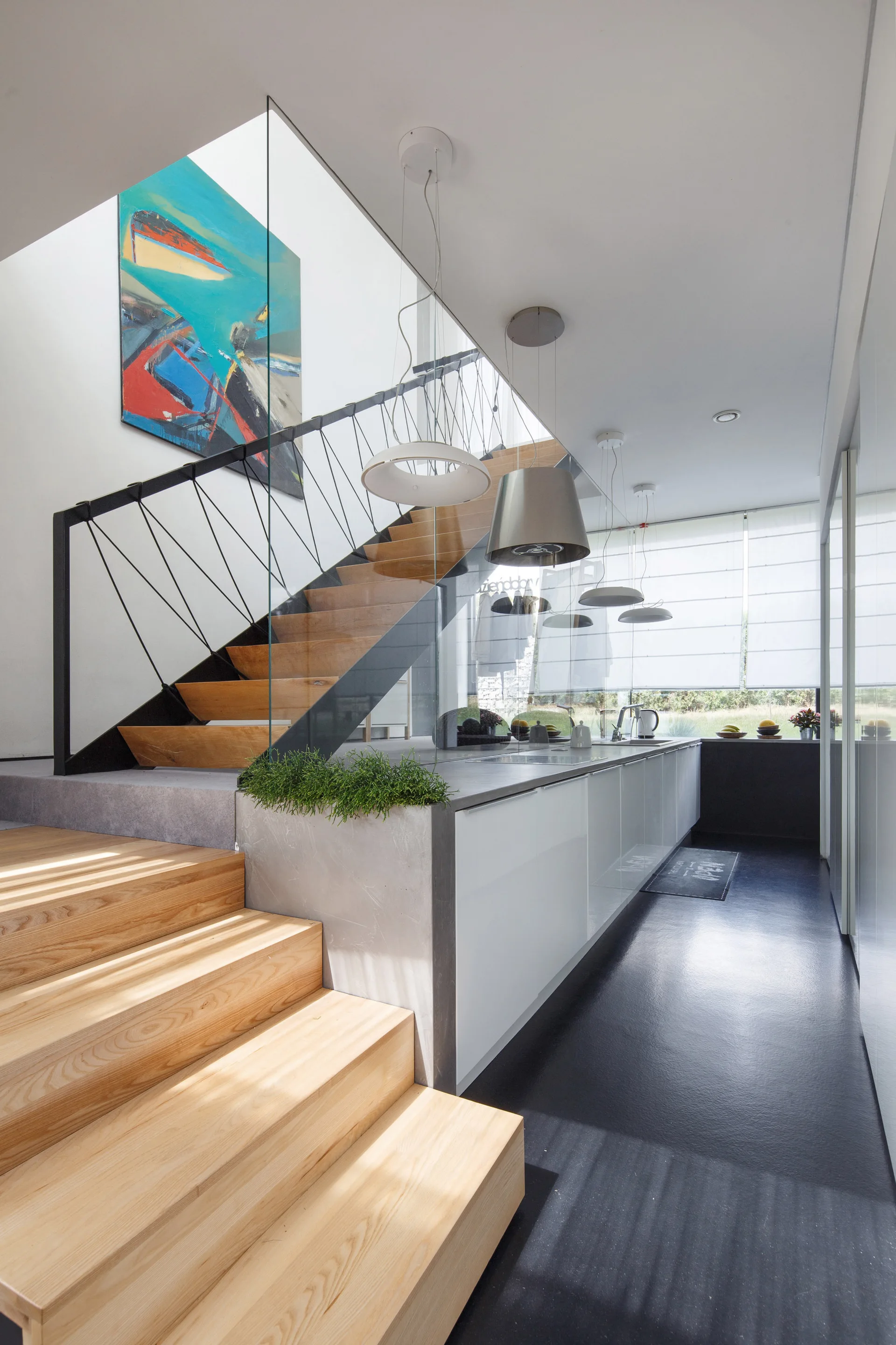 A modern kitchen with a glossy white island situated next to an open-tread wooden staircase with a clear glass partition.
