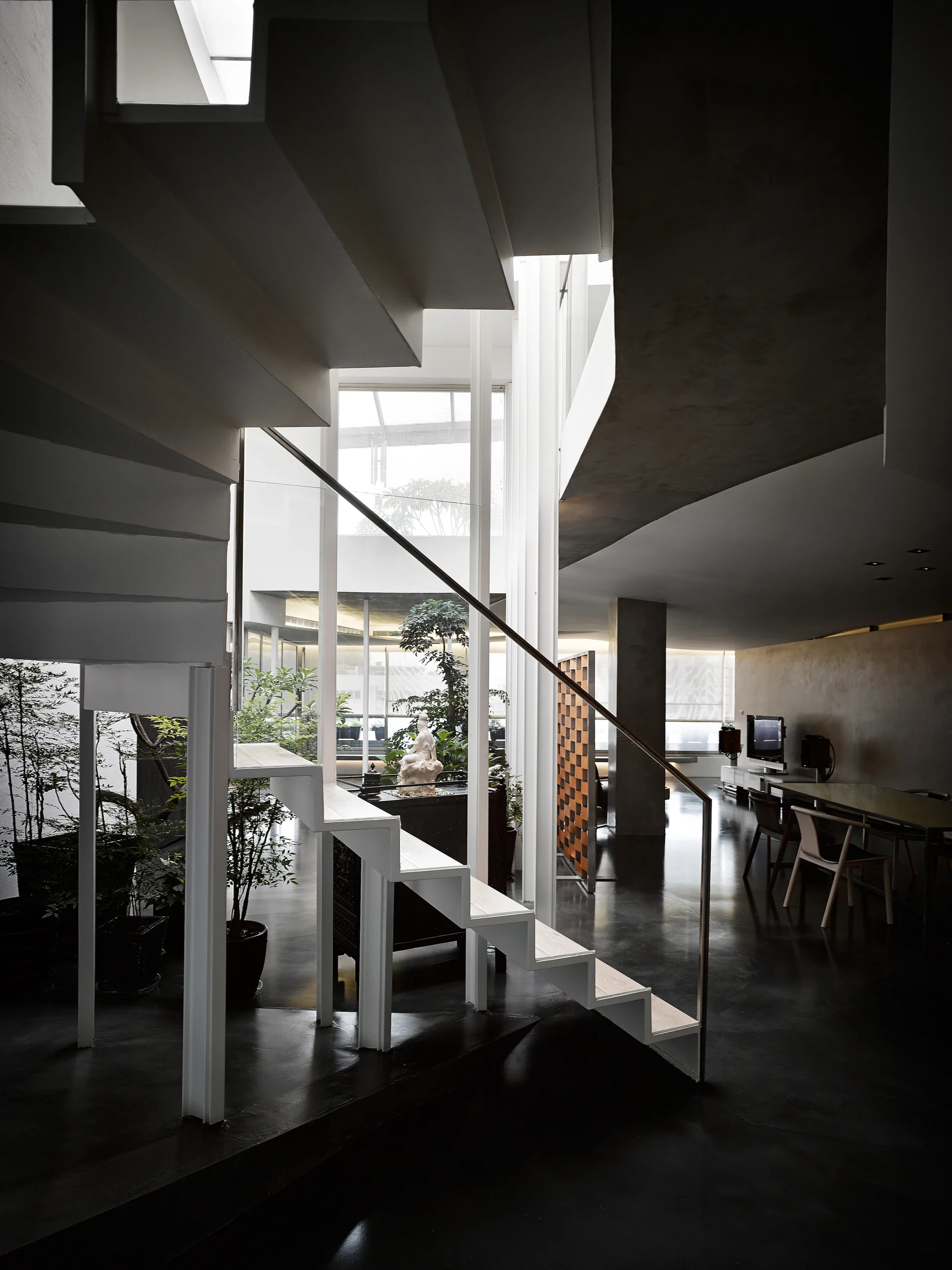 A white floating staircase with a slim handrail stands in a modern home with dark floors, large windows, indoor plants, and a dining table.