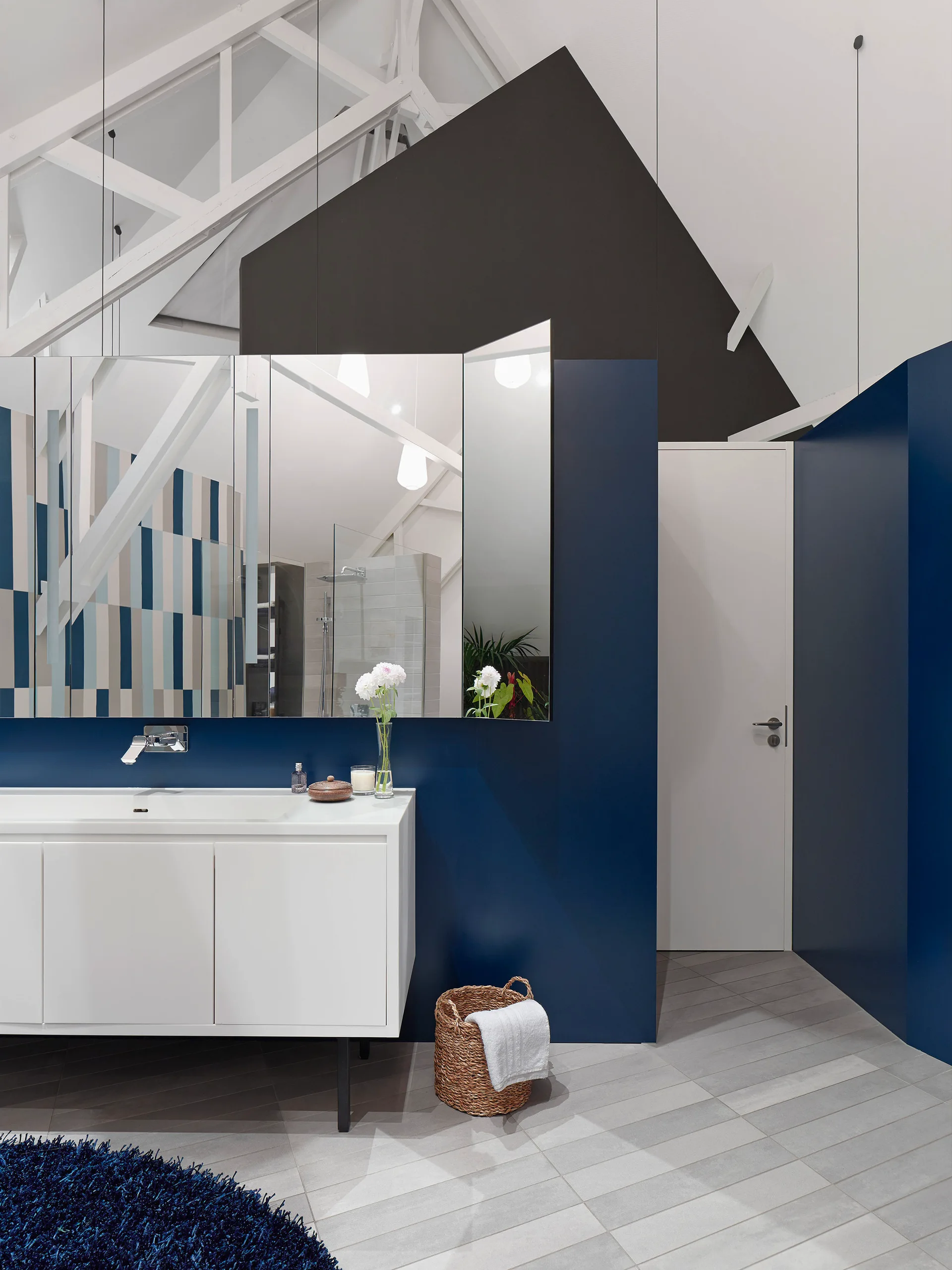 A modern bathroom features a white floating vanity against deep navy blue walls, a large mirror, and exposed white ceiling beams.