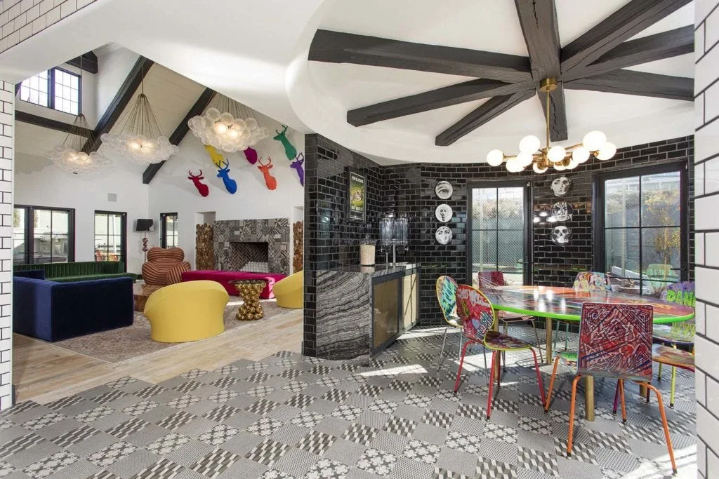 An eclectic dining space features black subway tile walls, geometric floor tiling, and a graffiti-patterned table next to an open-concept living area.
