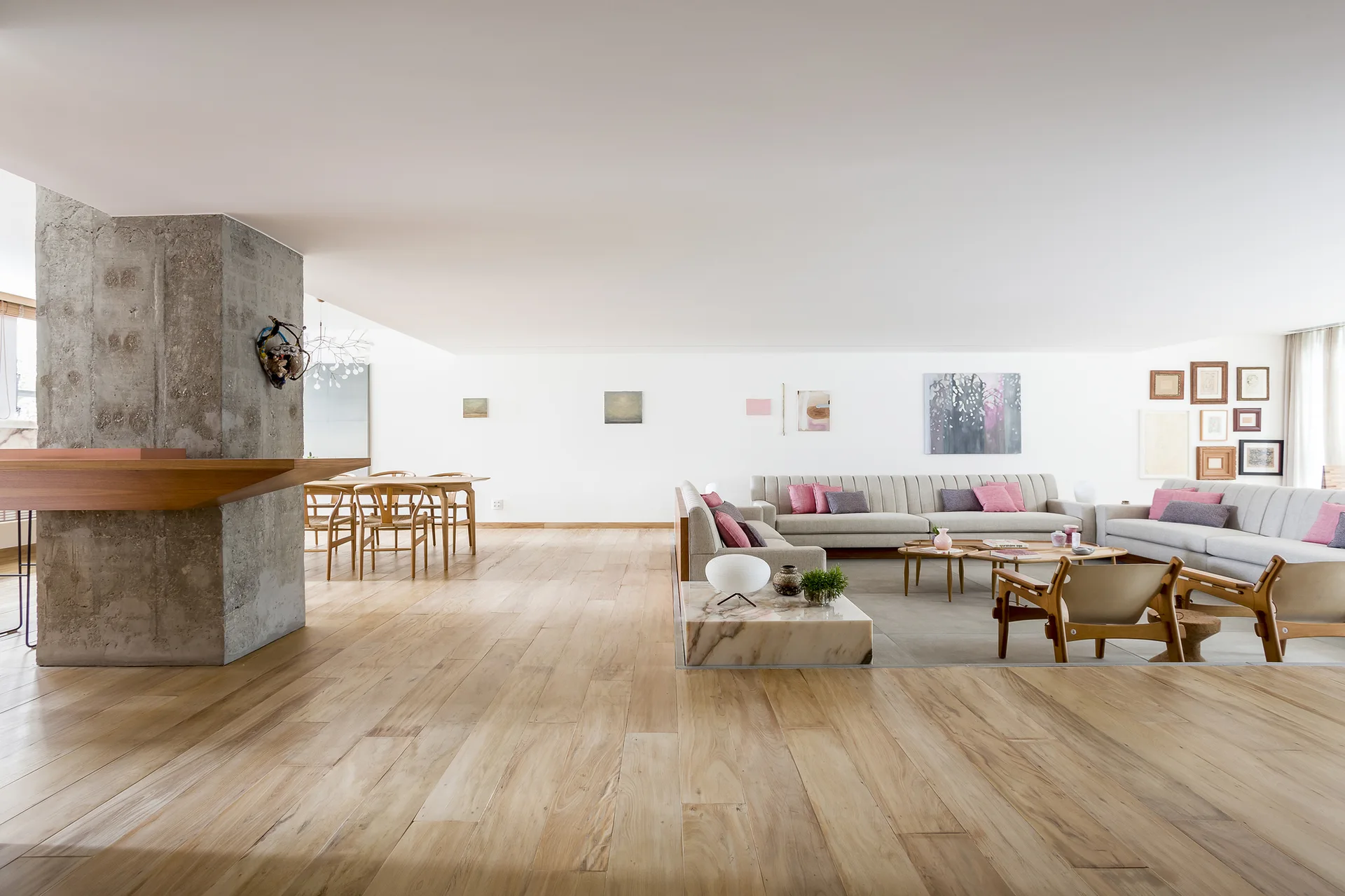 An open-concept living area features a large light gray sectional, a concrete support pillar, and light wood flooring extending to a dining space.