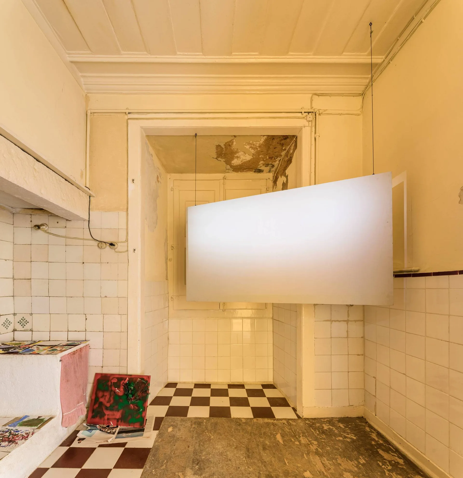 A rustic kitchen with a brown and white checkerboard tiled floor and a large white rectangular panel suspended from the ceiling.