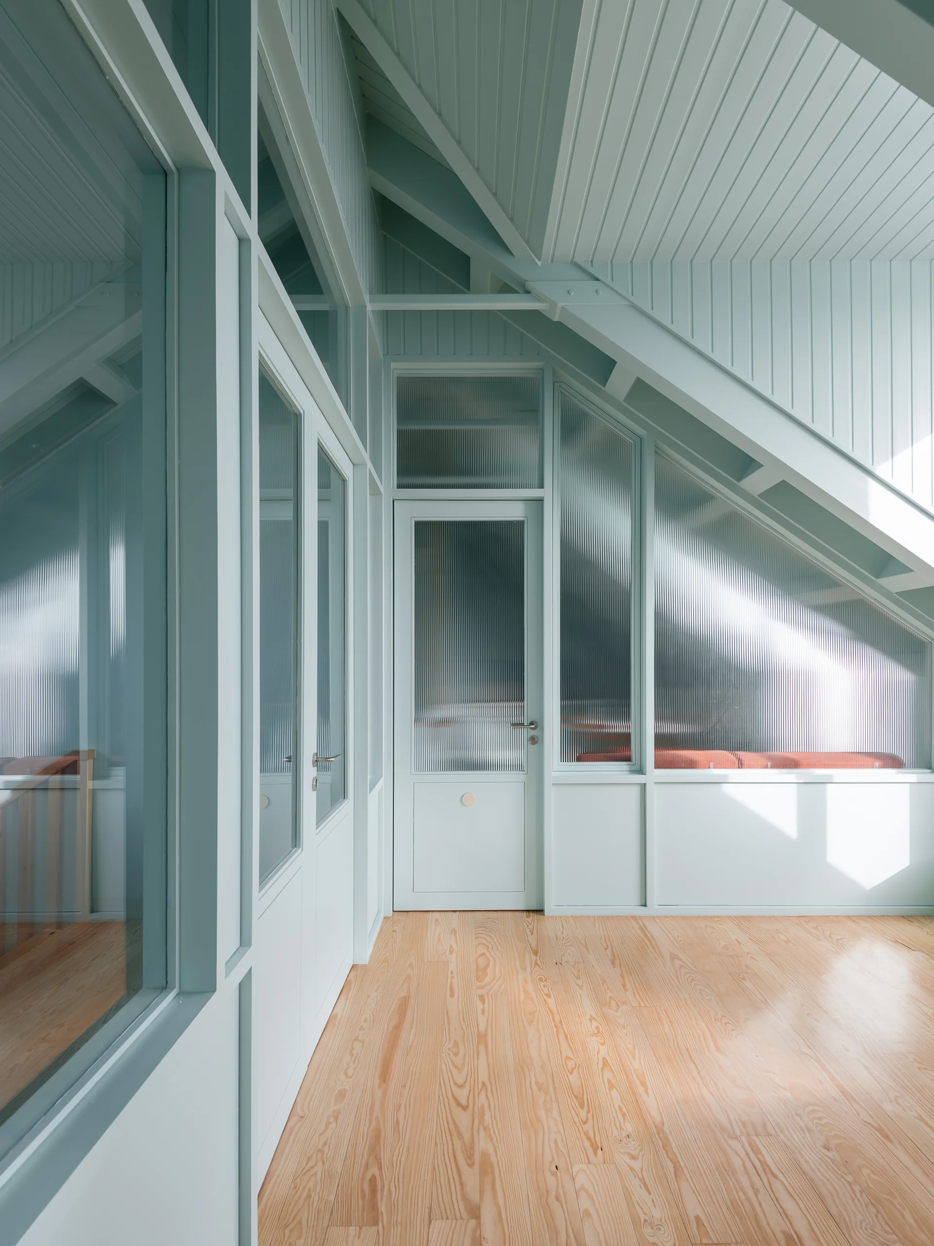 An attic hallway features light sage green painted paneled walls and ceiling, fluted glass doors, and light wood flooring.