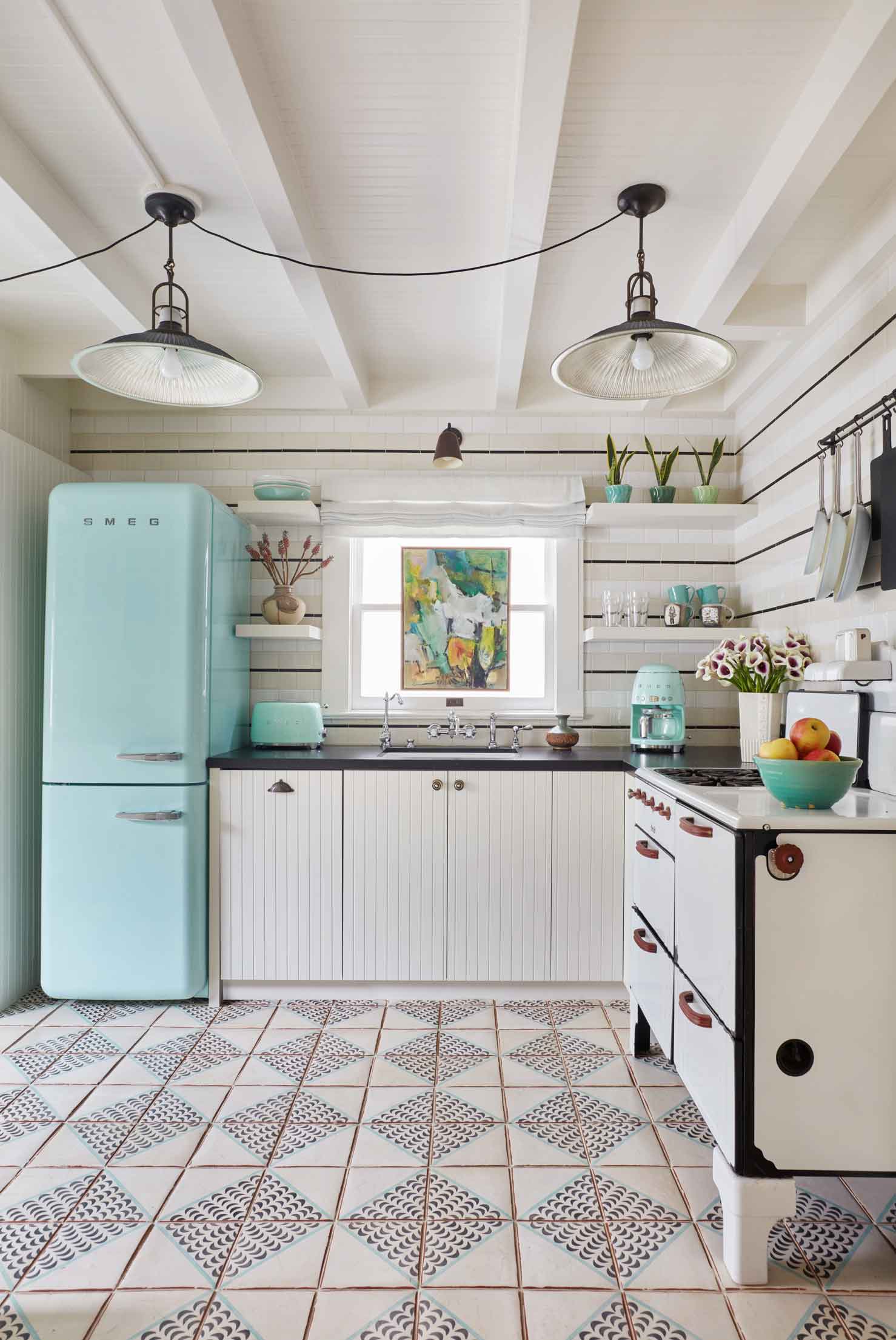 A bright kitchen features a pastel blue refrigerator, white cabinets, patterned floor tiles, and a backsplash with horizontal black stripes.