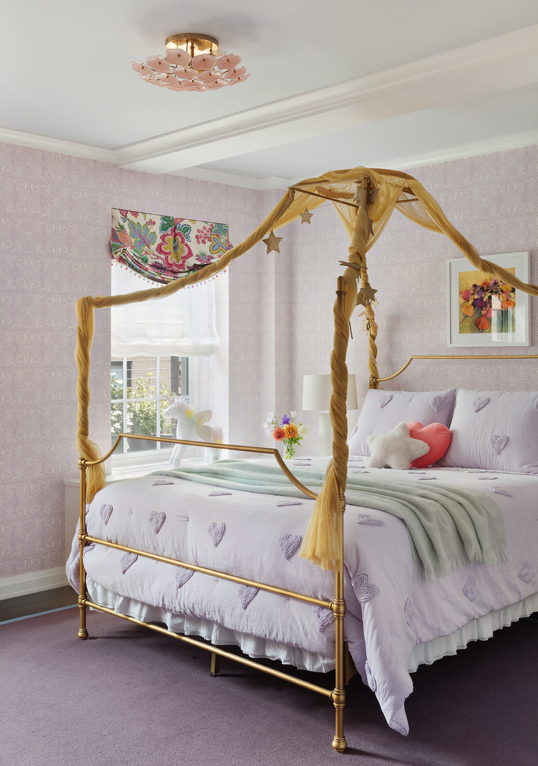 A children's bedroom featuring a gold four-poster canopy bed with purple heart-patterned bedding set against lavender wallpapered walls.