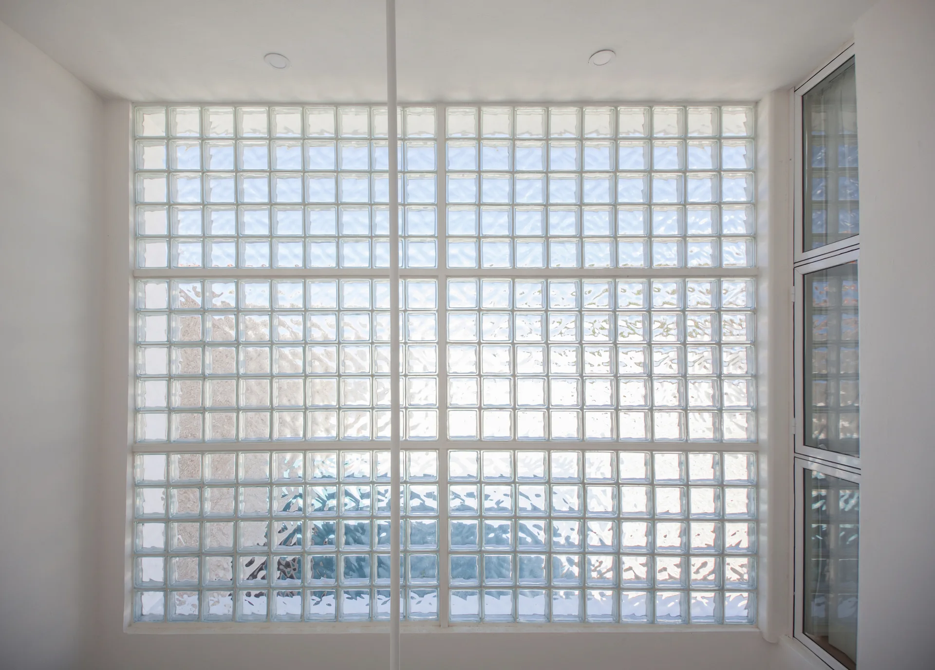 A large grid of translucent square glass blocks fills a white interior wall under a flat ceiling with recessed lights.