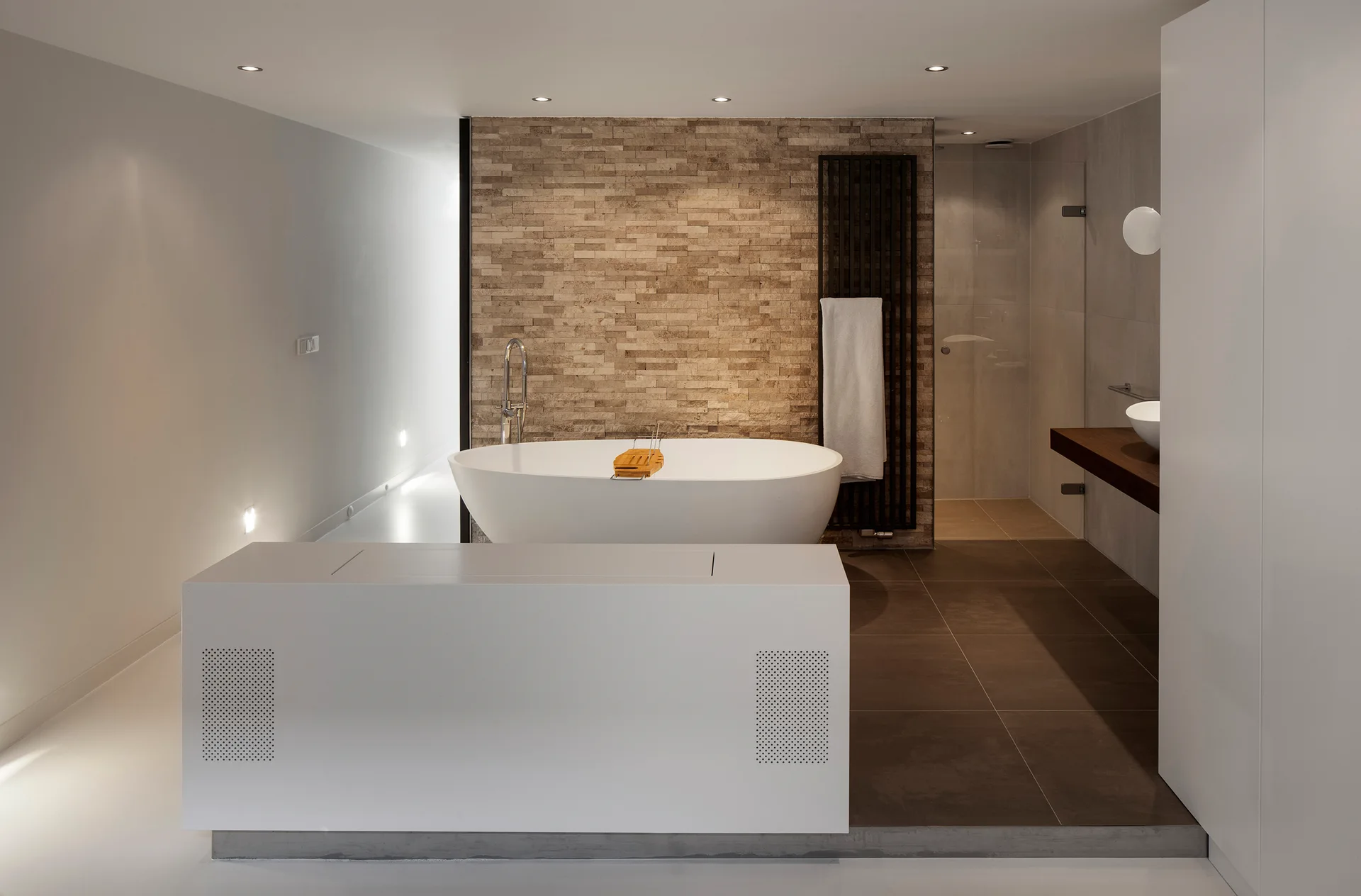 A modern bathroom features a white oval freestanding bathtub set against a textured stacked stone wall next to a dark tile shower area.