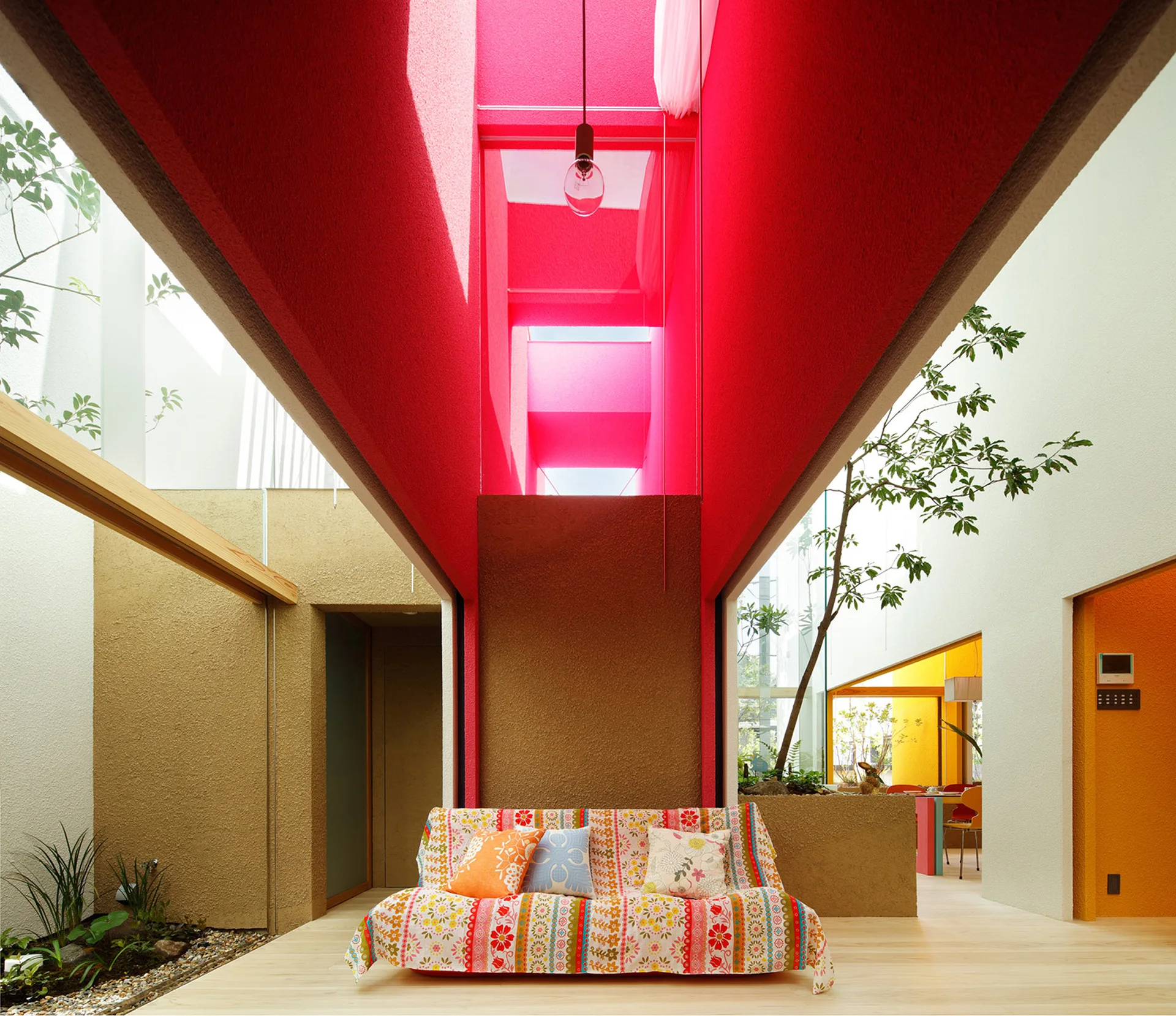 A patterned floral sofa sits under a towering, deep red skylight shaft in an open-plan living room with light wood floors.