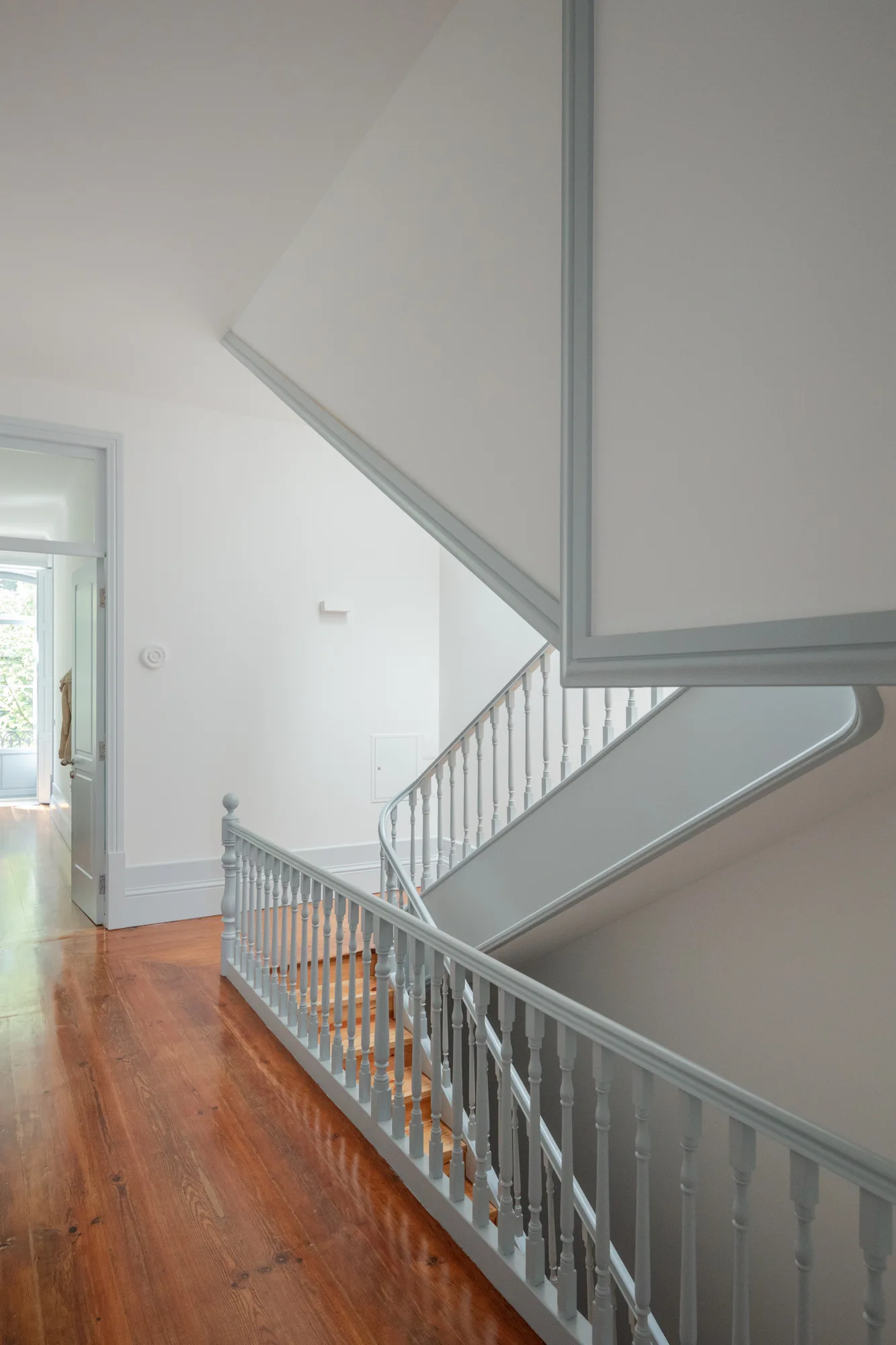 A traditional wooden staircase features a light grey painted spindle railing and polished warm wood treads set against clean white walls.