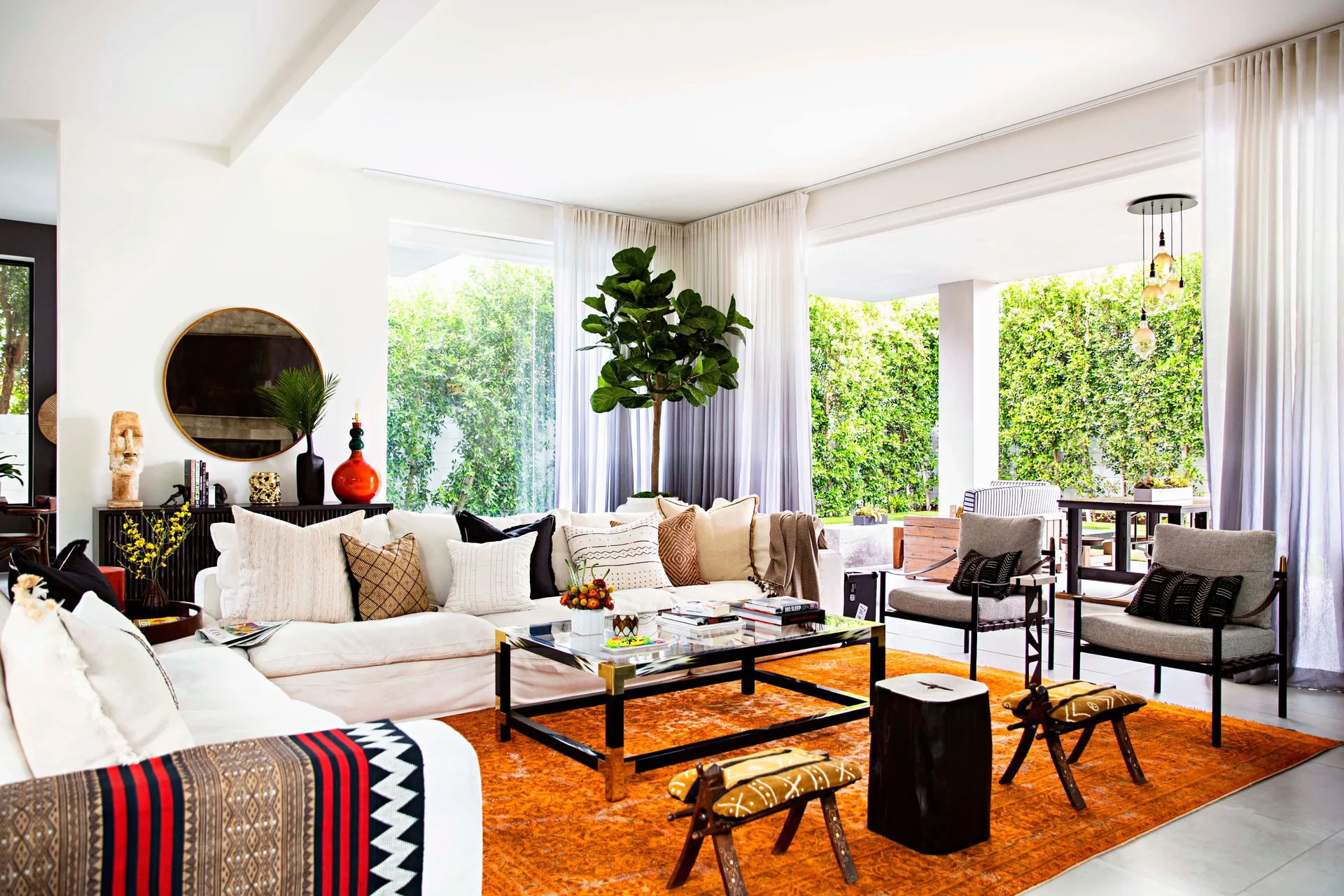 A bright living room features a cream sectional sofa, a large burnt orange rug, and floor-to-ceiling glass doors opening to a patio.