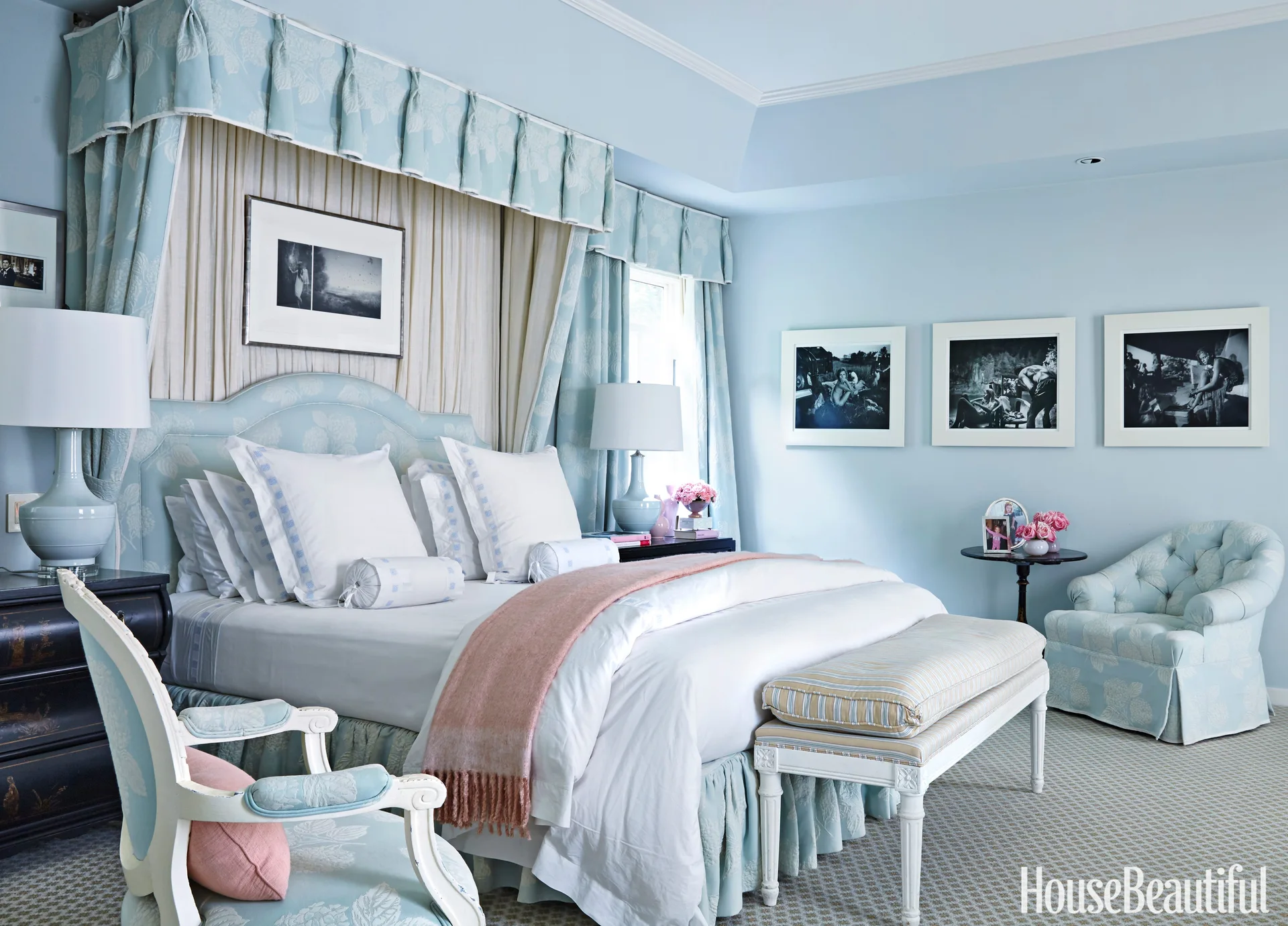 A traditional blue bedroom features an upholstered canopy bed with matching floral drapery, dark wood nightstands, and a tufted armchair.