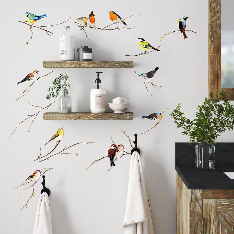 Rustic wooden floating shelves and black towel hooks share a white bathroom wall decorated with colorful bird decals next to a wood vanity.