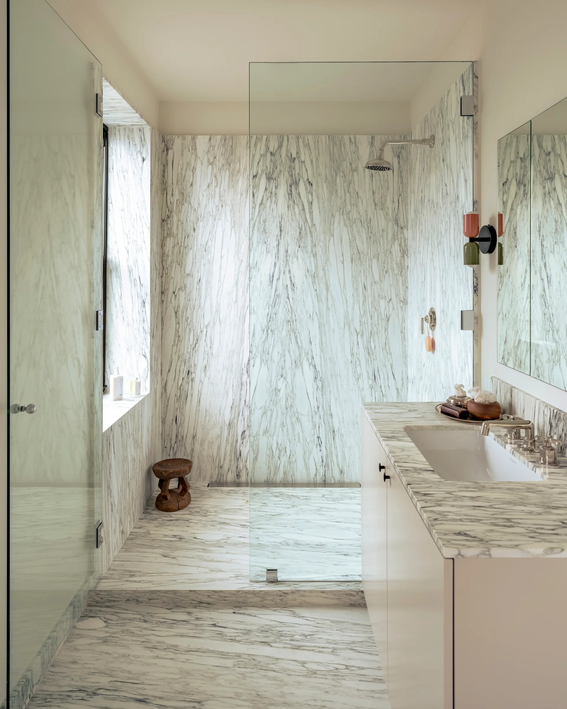 A modern bathroom featuring walls and floors clad in heavily veined marble, a glass walk-in shower, and a white vanity with a matching marble countertop.