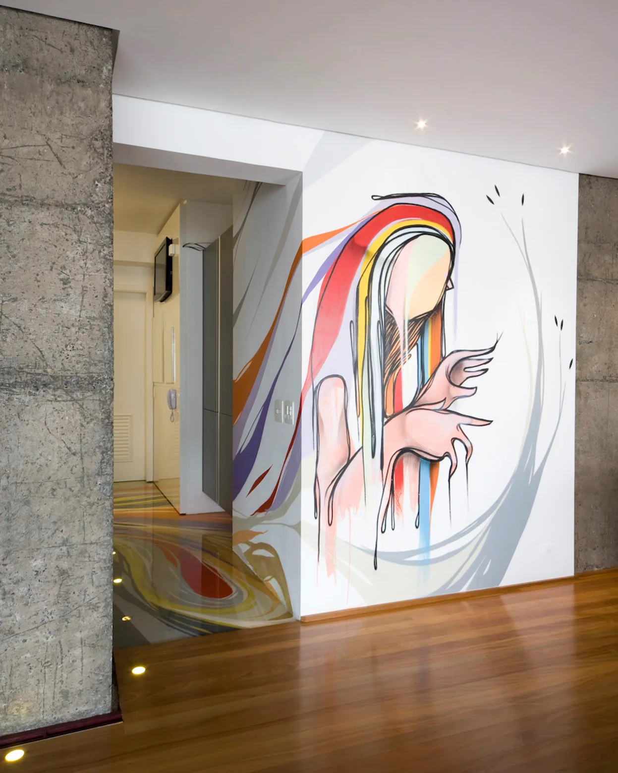 A modern hallway featuring a large colorful wall mural of a figure next to an exposed raw concrete pillar and polished wood flooring.