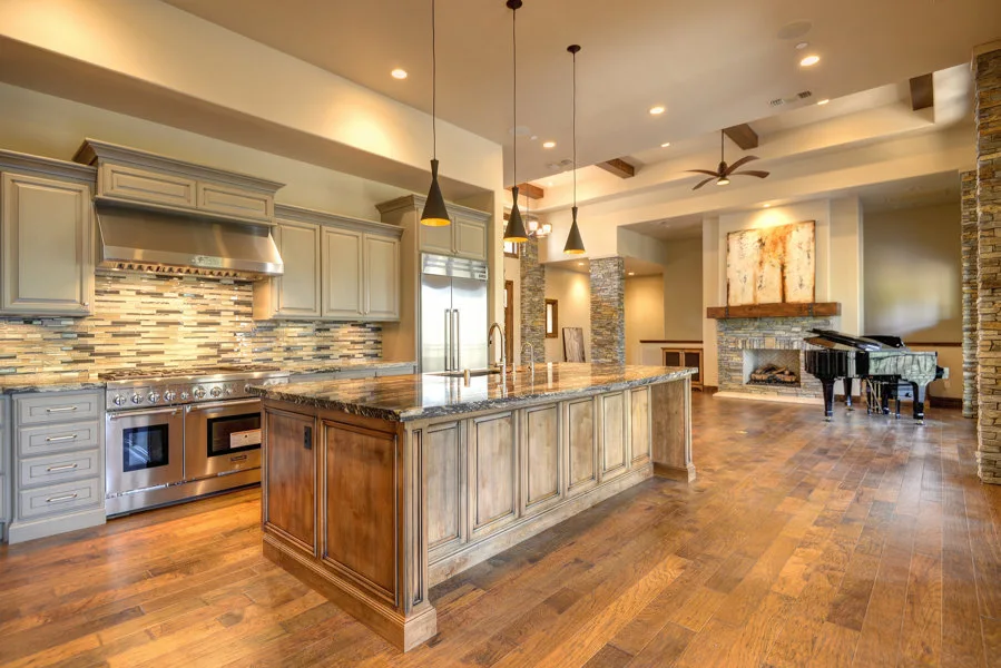 A spacious kitchen with grey cabinetry, a large warm wood island, stainless steel appliances, and hardwood floors.
