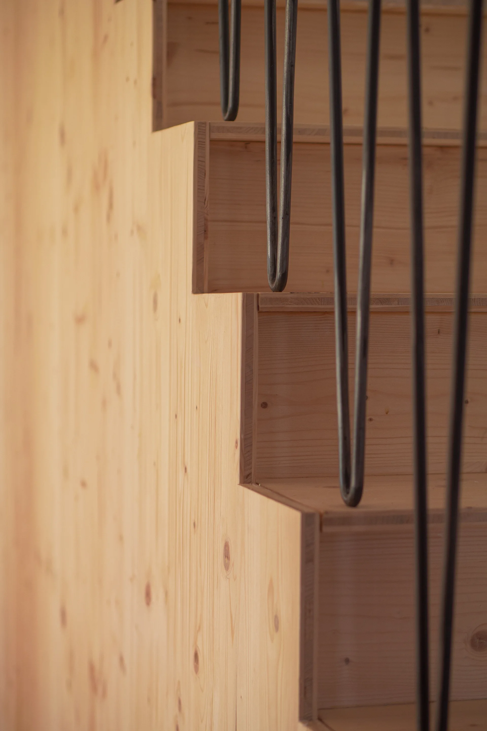 A close-up of a minimalist wooden staircase made of light-toned pine with thin black metal balusters attached to the steps.