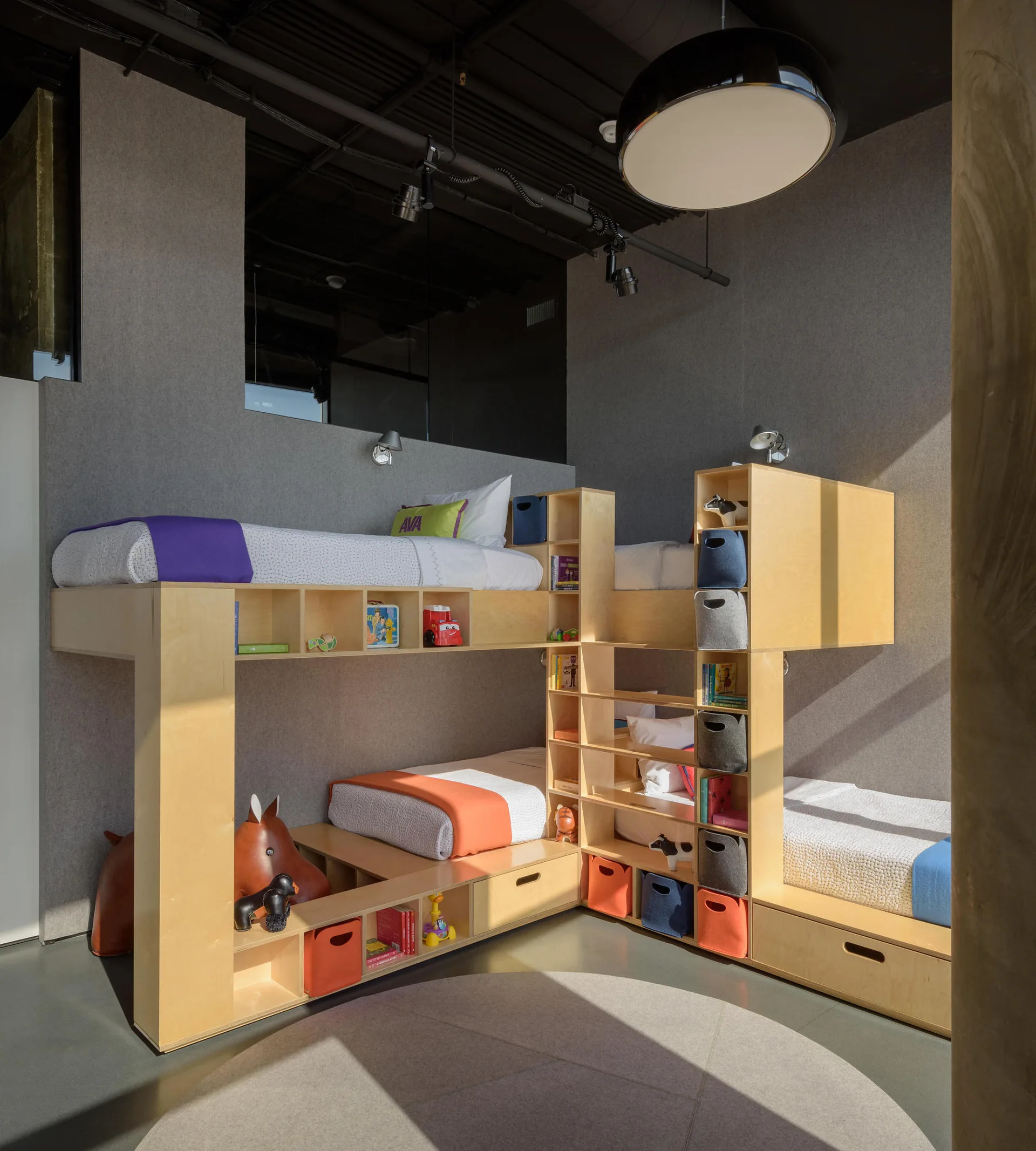 An L-shaped light wood bunk bed system features built-in storage cubbies, colorful fabric bins, and grey wall panels in a child's bedroom.