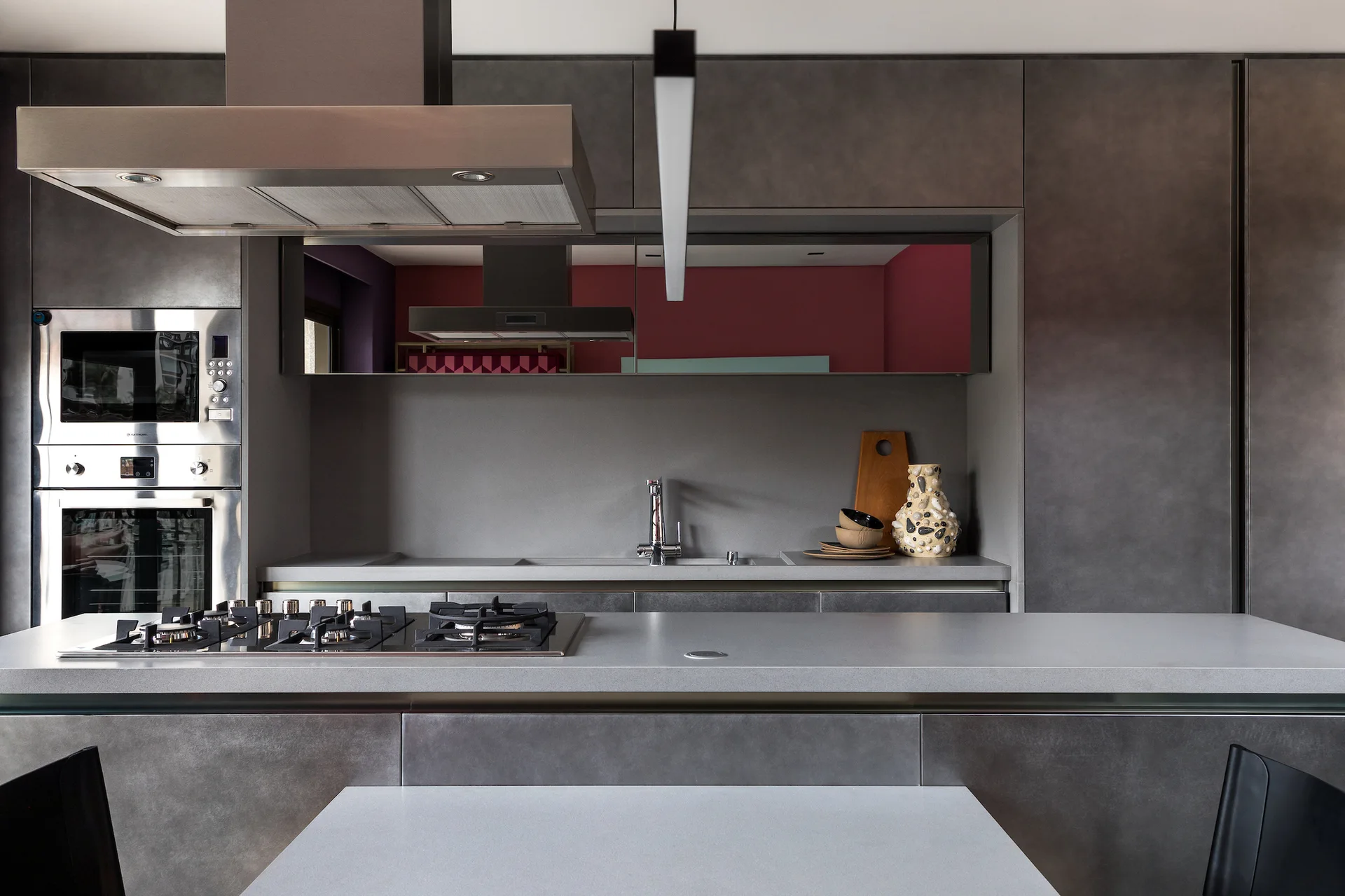 A modern gray kitchen features matte cabinetry, a stainless steel range hood, a kitchen island with a gas cooktop, and a reflective mirrored backsplash.