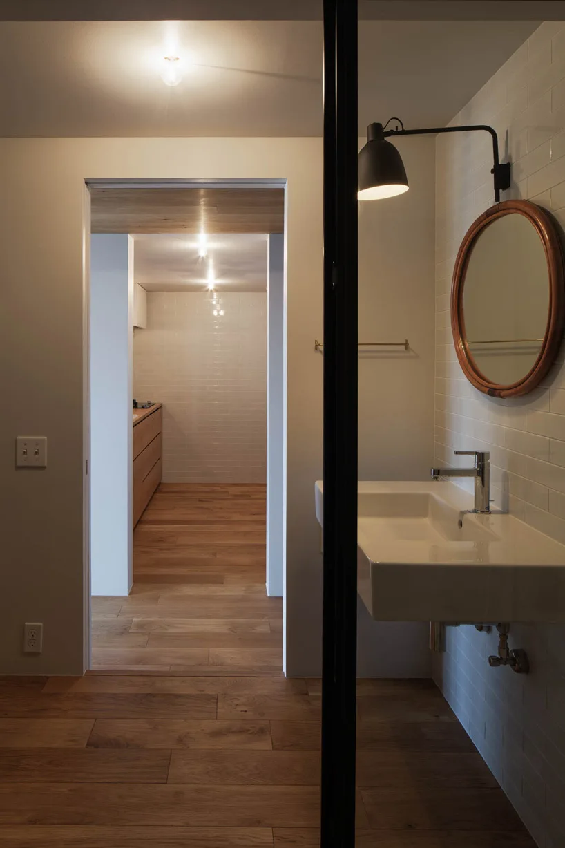 White subway tile bathroom featuring a floating white sink, a round wood-framed mirror, a black wall sconce, and wood flooring.