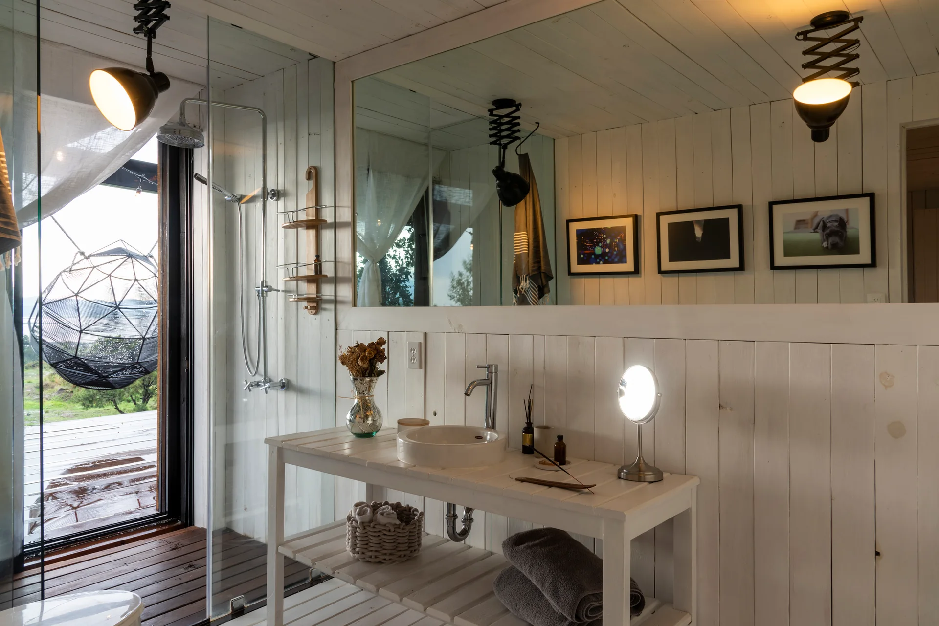 A rustic bathroom features white vertical wood plank walls, an open slatted vanity with a round vessel sink, and a large rectangular mirror.