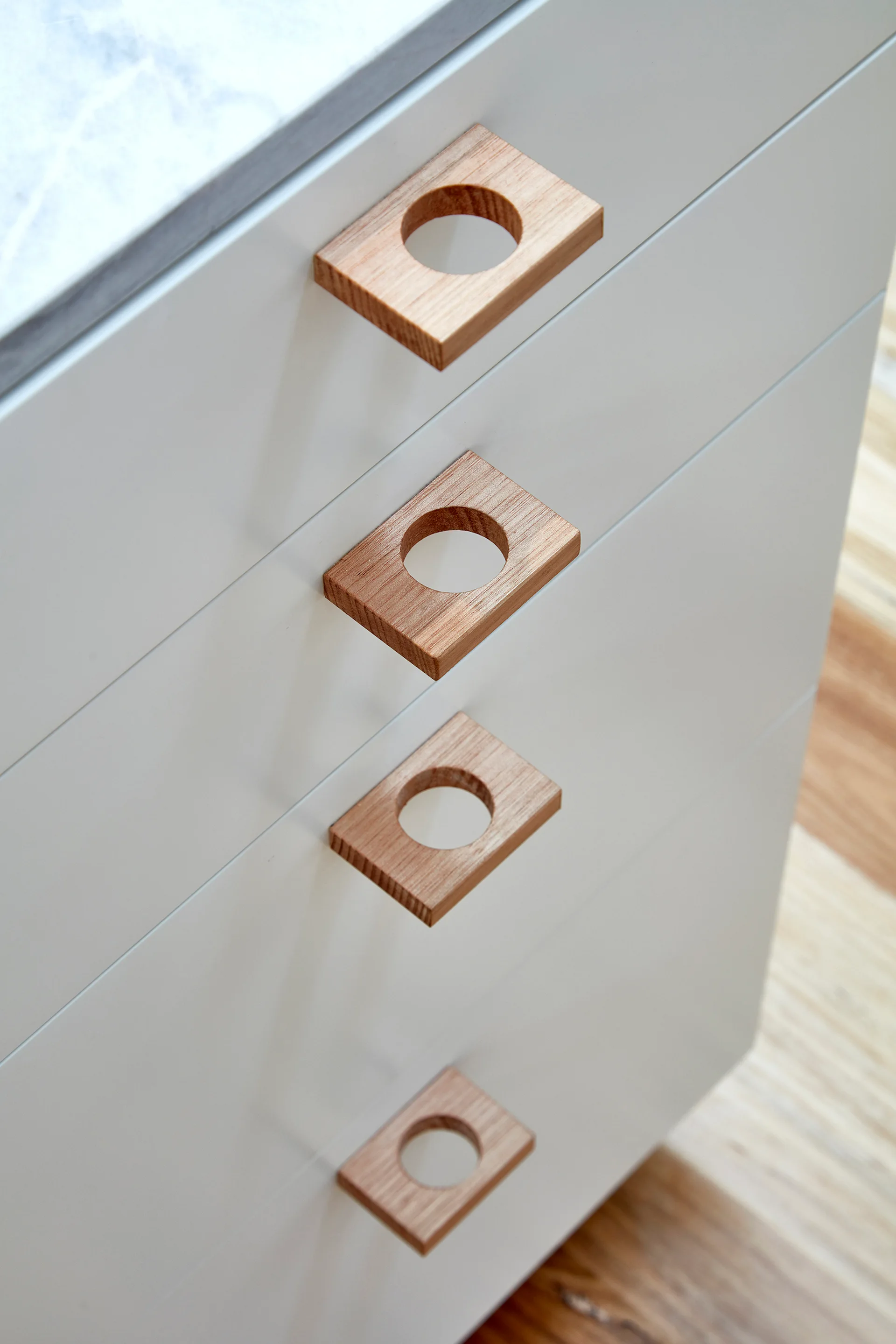 A close-up of four white drawers featuring rectangular light wood handles with circular cutouts.
