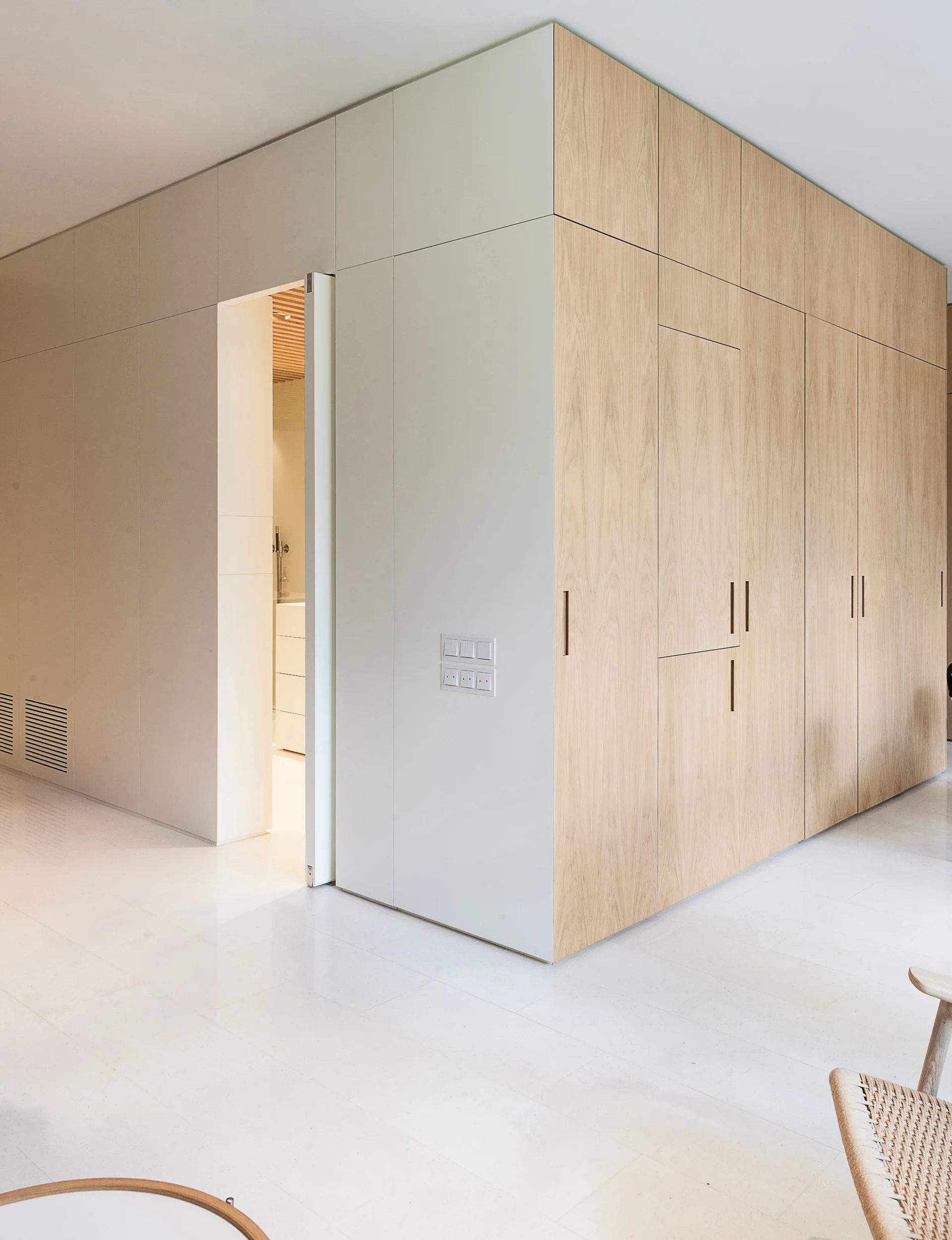Custom floor-to-ceiling cabinetry with white and light wood panels surrounds a doorway above a smooth light stone floor.